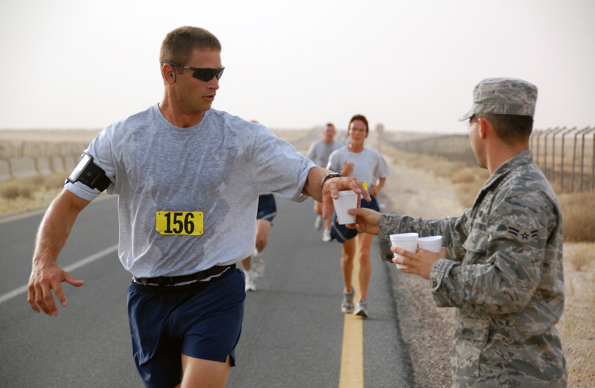 U.S. Air Force Staff Sgt. Dennis Barnhart of the 386th Expeditionary Civil Engineer Squadron takes a cup of water from Airman 1st Class Derek Cruz of the 386th Expeditionary Force Support Squadron at the turnaround point of a Memorial Day 10K fun run at an air base in Southwest Asia. Sergeant Barnhart placed second in the 30-39 year-old category at 47:00. (U.S. Air Force photo by Tech. Sgt. Lindsey Maurice/Released)