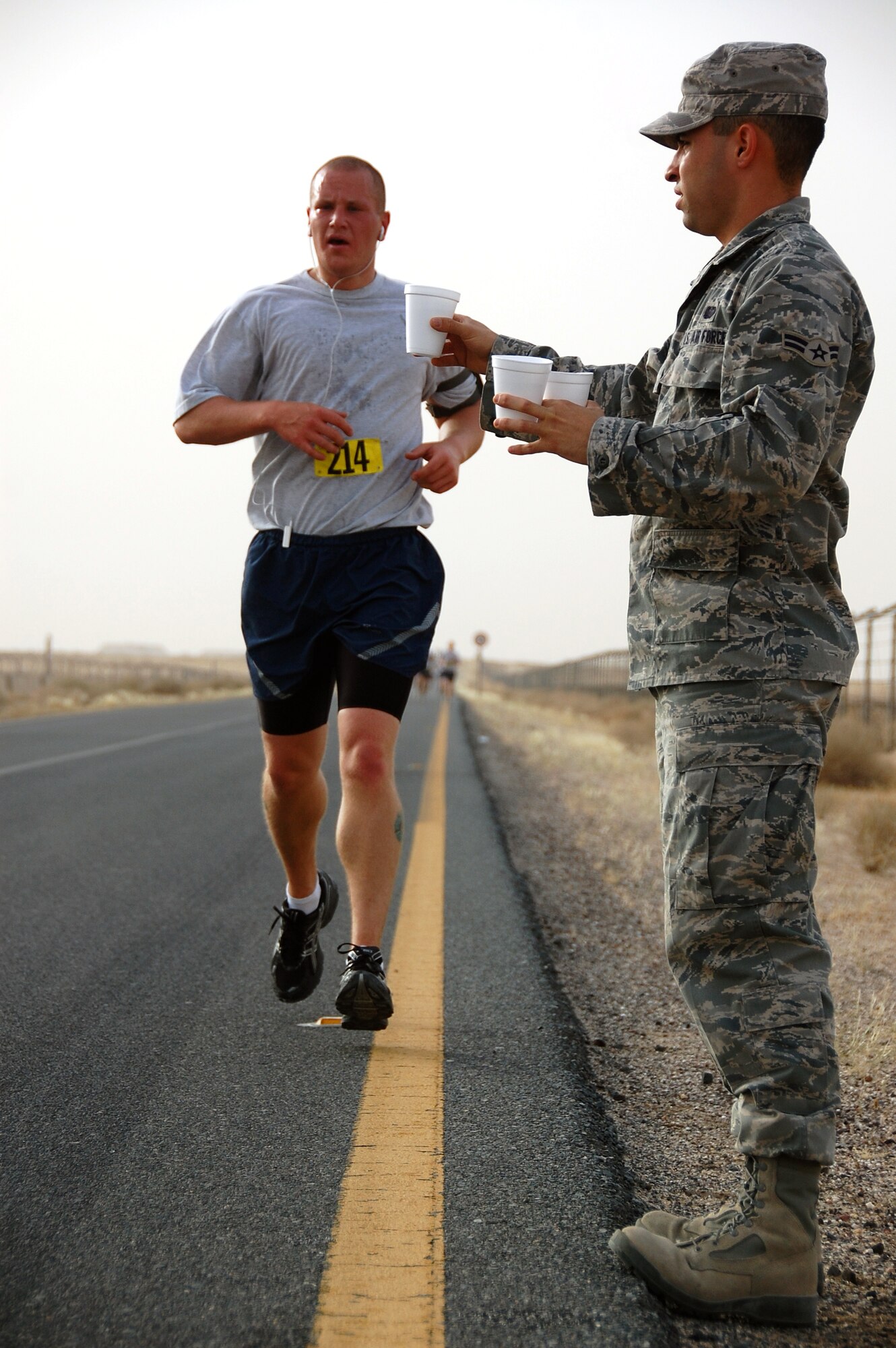U.S. Air Force Airman 1st Class Derek Cruz of the 386th Expeditionary Force Support Squadron holds out a cup of water for Senior Airman Chad Keever of the 386th Expeditionary Security Forces Squadron at the turnaround point of a Memorial Day 10K fun run May 31, 2010 at an air base in Southwest Asia. The 386th EFSS fitness center staff hosted the early morning run with the help of volunteers. (U.S. Air Force photo by Tech. Sgt. Lindsey Maurice/Released)