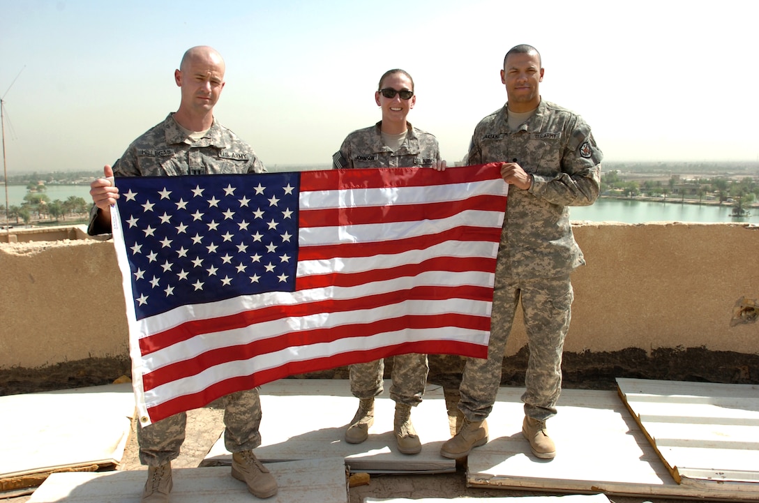 From left  to right, U.S. Army Capt. Nathan Hillegas, Capt. Kindall Johnson and Spc. Patrick Williams hold a flag up as servicemembers and Department of Defense civilians gather at the top of the Victory Over America Palace in Baghdad to unveil U.S. flags in honor of Memorial Day, May 31, 2010.