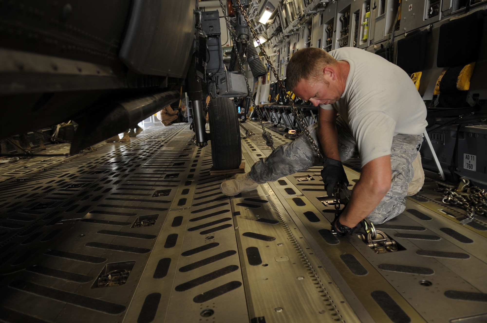 Staff Sgt. Jason Paul, 55th Helicopter Maintenance Unit, ties down a chain from a folded HH-60G Pave Hawk onto the floor of a C-17 Globemaster III May 25 at Kandahar Airfield, Afghanistan.  Each small tie-down chain is rated at holding 10,000lbs and the larger tie-down chains gold 25,000lbs.  (U.S. Air Force photo by Senior Airman Nancy Hooks/Released))