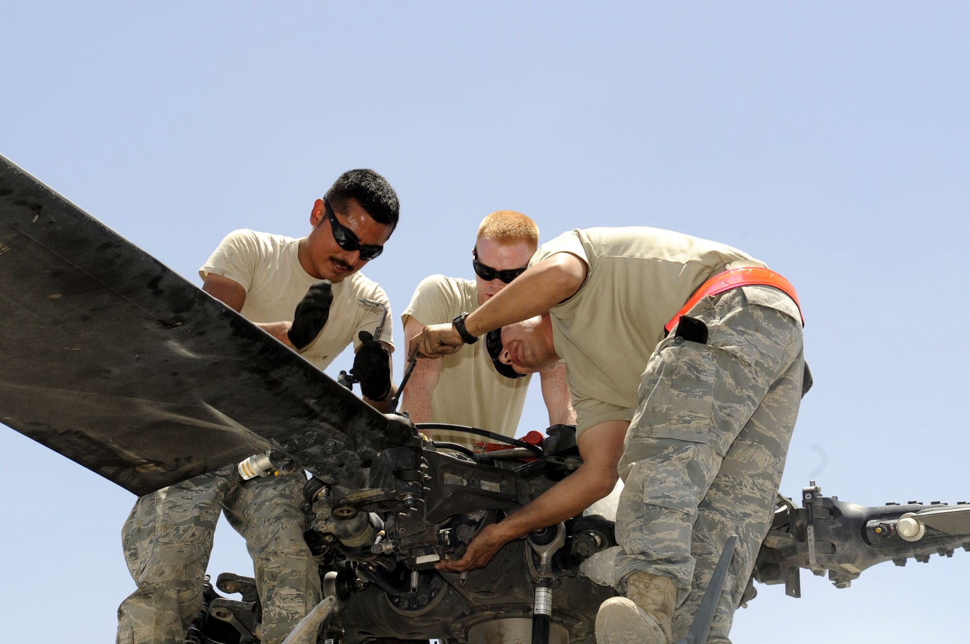 Senior Airman Mark Mark Cadena, Reid Cecil, and Staff Sgt. Earl Radel remove a main rotor blade retaining pin May 19 while folding a HH-60G Pave Hawk for air shipment at Kandahar Airfield.  Members of the 451st Aircraft Maintenance Squadron work together as a team while preparing the aircraft for transport.  (U.S. Air Force photo by Senior Airman Nancy Hooks/Released)