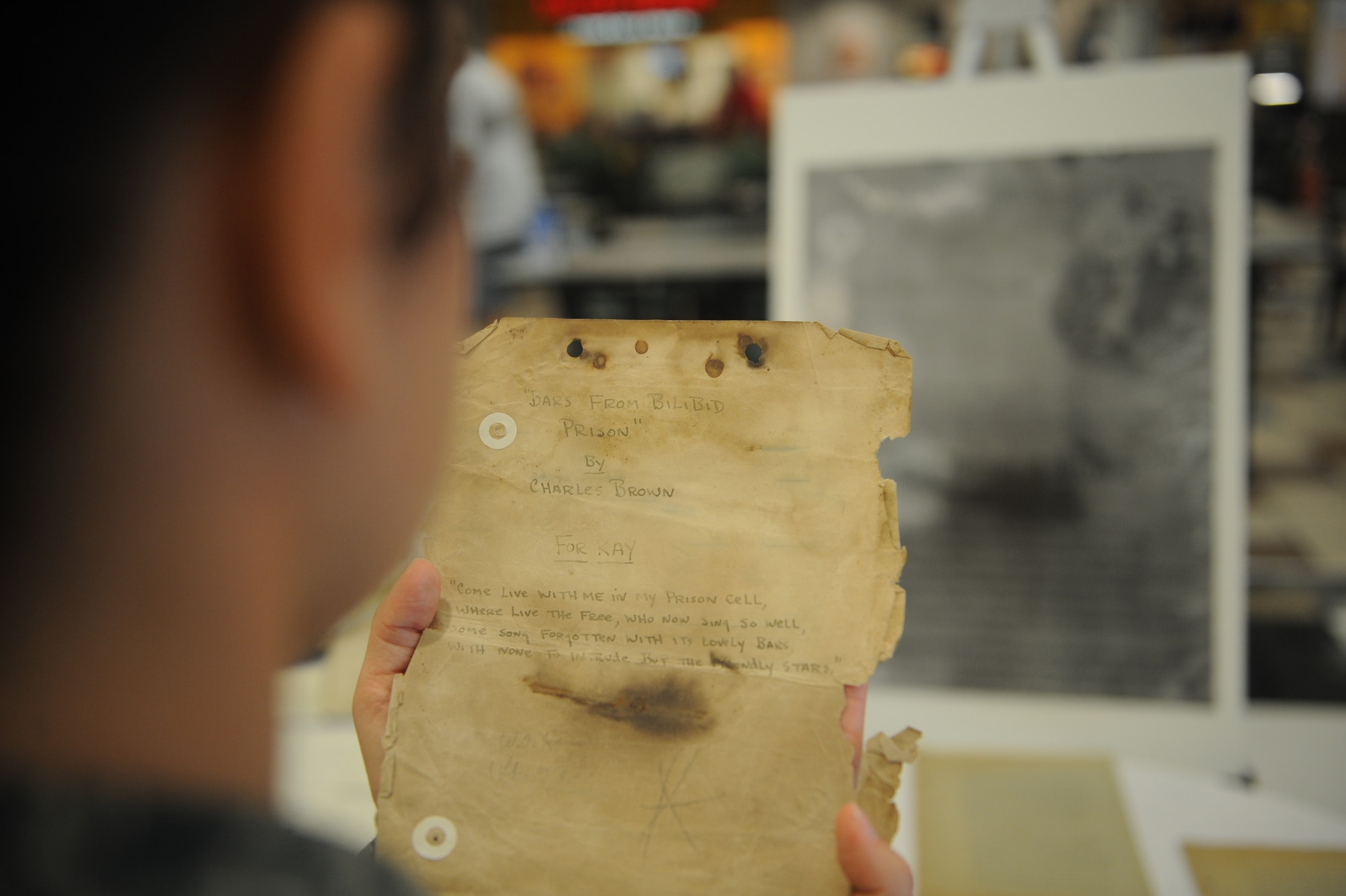 DYESS AIR FORCE BASE, Texas-- A Dyess Airman holds the original cover page of Charles Brown's collection of poems, "Bars from Bilibid Prison," June 2 at the Dyess Base Exchange here. Charles Brown was a Prisoner of War for three years in Bilibid prison Muntinlupa City, Philippines, during World War II.  Charles Brown wrote 90 poems and kept them hidden from the Japanese throughout his imprisonment. According to Blair Howell, founder and present owner of the collection, the display of Brown's original poems at the base exchange will remain for a couple weeks. (U.S Air Force photo/ Airman 1st Class Shannon Hall)