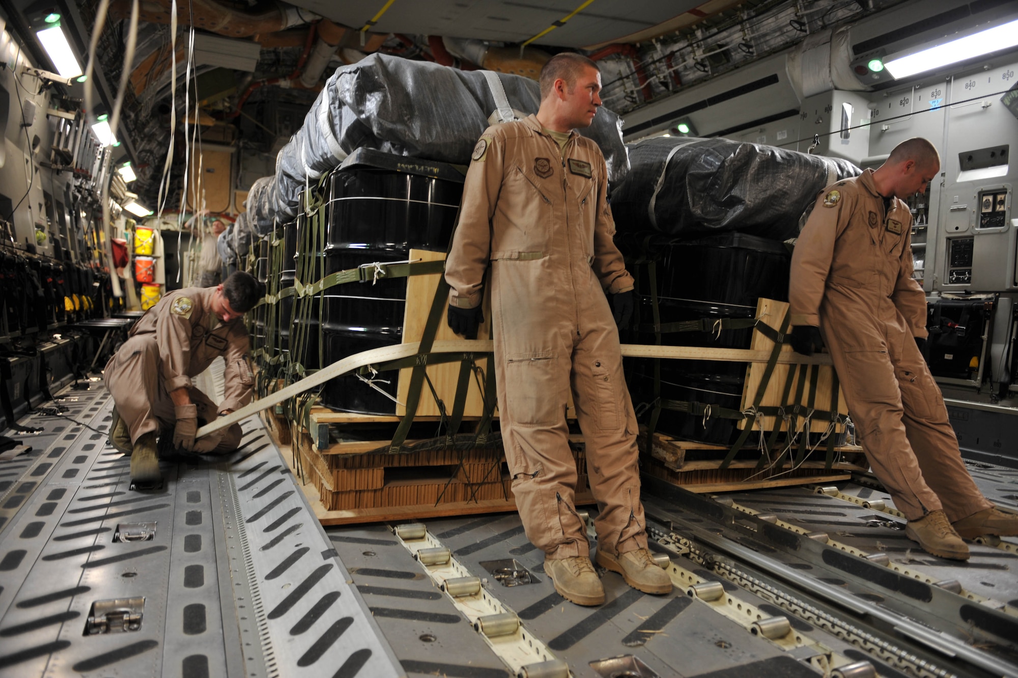 U.S. Air Force loadmaster Senior Airman Josh Faust, left, straps container delivery system bundles to the floor of a C-17 Globemaster III, while loadmaster Staff Sgt. Gabriel Reams, center, and pilot Capt. Dave Goodale hold the bundles in place at Kandahar Airfield, Afghanistan, May 27, 2010.  The crew released the bundles over Afghanistan, resupplying the Combined Joint Special Operations Task Force with food, water and fuel.  Captain Goodale, Sergeant Reams and Airman Faust are assigned to the 816th Expeditionary Airlift Squadron.  (U.S. Air Force photo/Staff Sgt. Quinton Russ/released)
