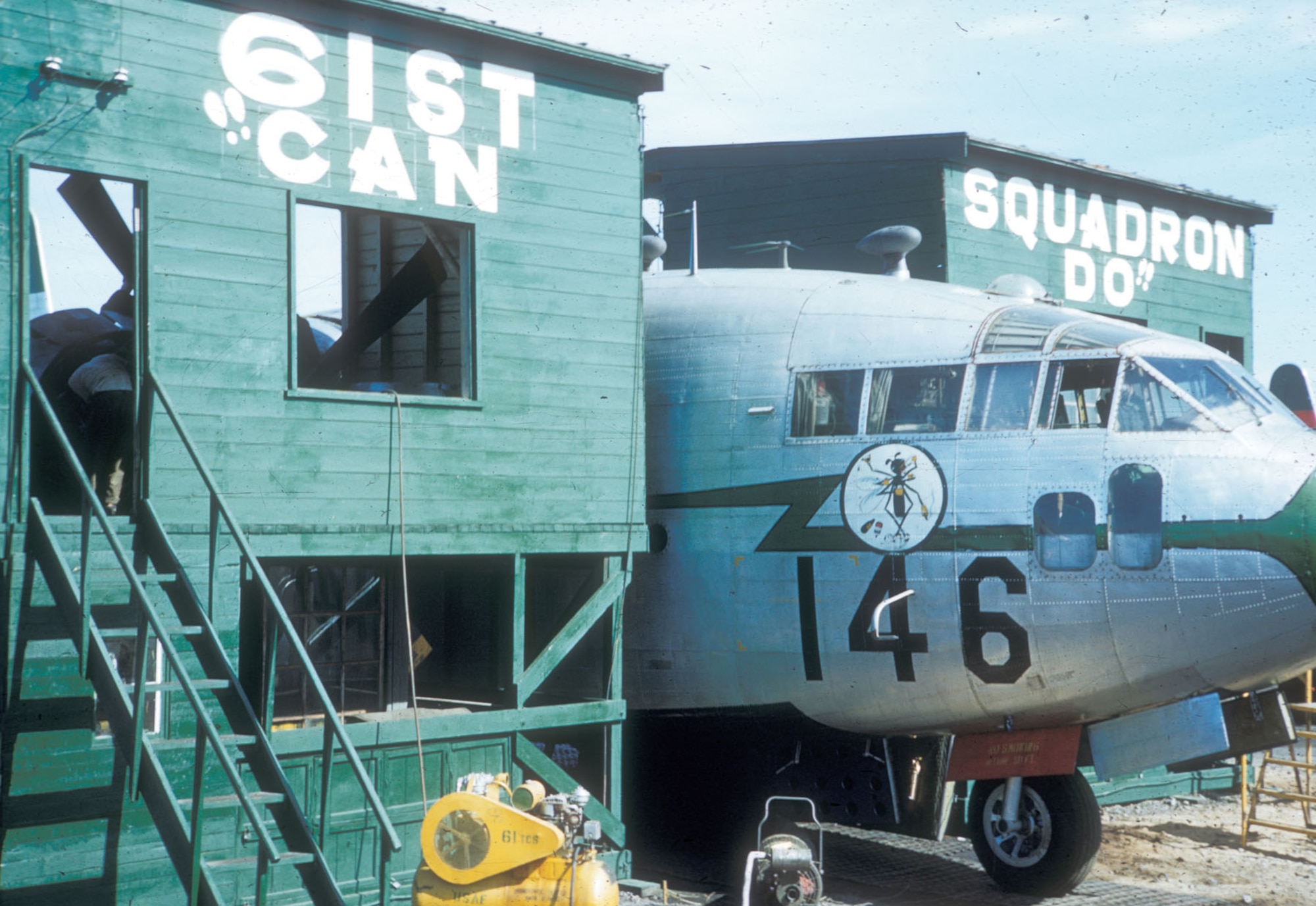 The 61st Troop Carrier Squadron dealt with the lack of hangars with their “Can-Do” spirit. When a C-119 was pulled up to these custom-built stands, a mechanic had a work platform and some shelter against the elements. (U.S. Air Force photo)