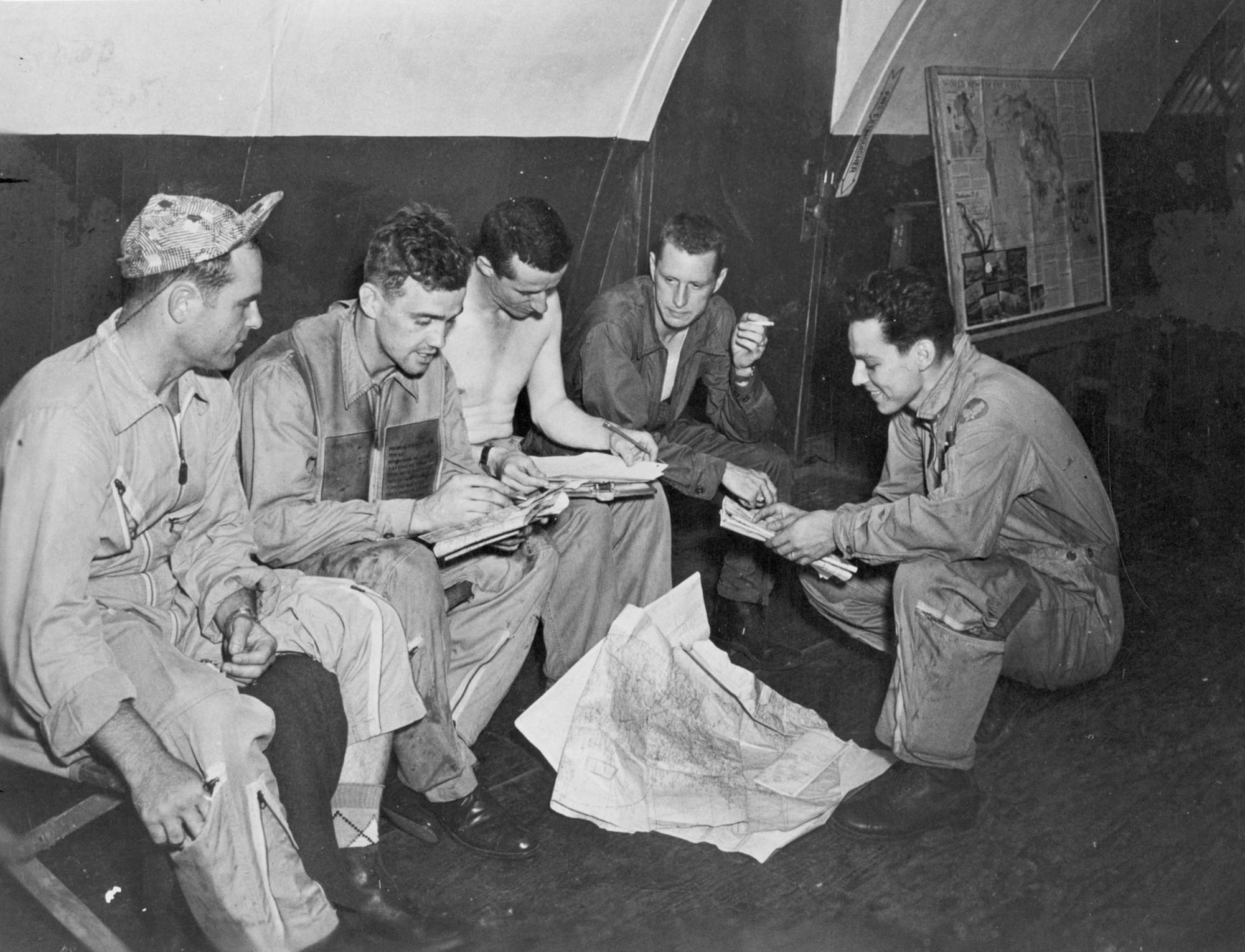 First on the left is Lt. Charles Moran. In the center is a sergeant writing out an intelligence report on the aerial battle. Second from the right is Lt. William Hudson.  Stooping is Lt. Carl Fraser, the radar operator who flew with Hudson. (U.S. Air Force photo)