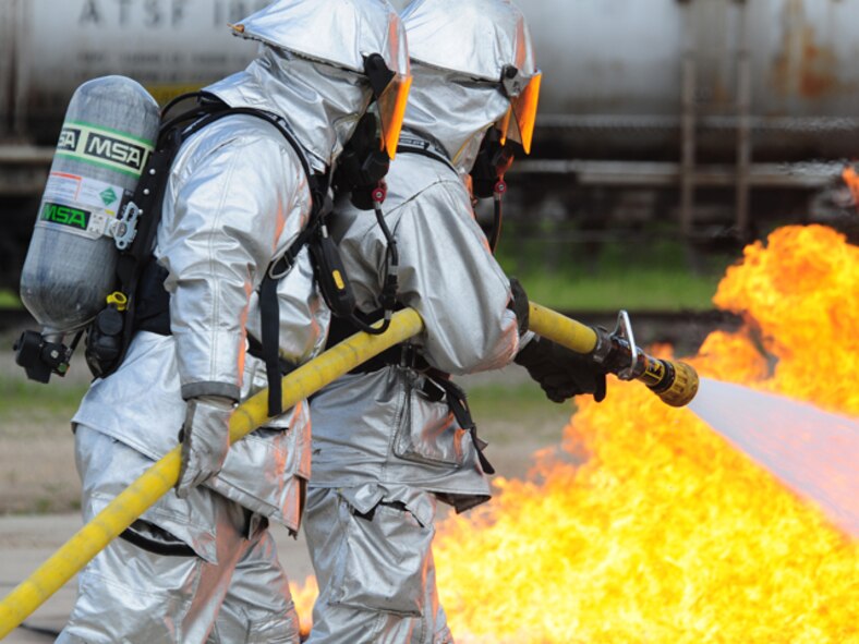 Tech. Sgt. Jesse Schmidt leads Staff Sgt. Erik Vosseteig, both of the 119th Civil Engineer Squadron, on a two-person hose team June 6, as they approach a mock aircraft burn pit while performing fire fighter training at the North Dakota Air National Guard Regional Training Site, Fargo, N.D.  The mock aircraft burn pit provides realistic training for the fire fighters with technically controlled flames emanating from various areas of a metal airplane frame.