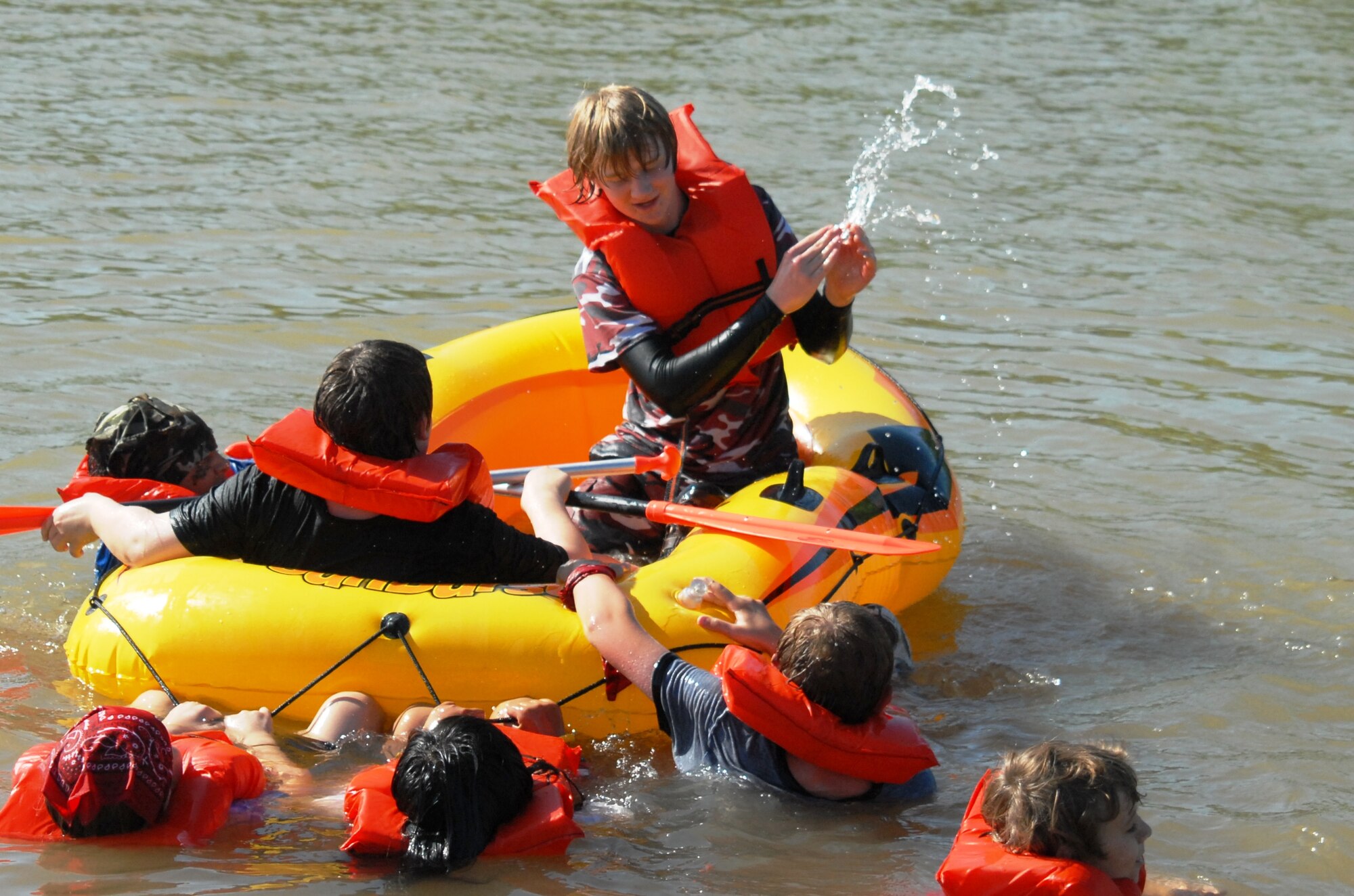 Tom Zimmerman, 15, bails out water while members from both tribes, Red and Camo, enjoy some down time waiting for their next challenge during the Youth Center's 9th Annual Survivor Weekend June 4-6 at Hot Water Slough Park. Fourteen youth ages 9-18 spent three days competing in "Survivor" challenges that tested their strength and taught them problem solving skills, team work and self confidence. (U.S. Air Force photo/Connie Hempel)