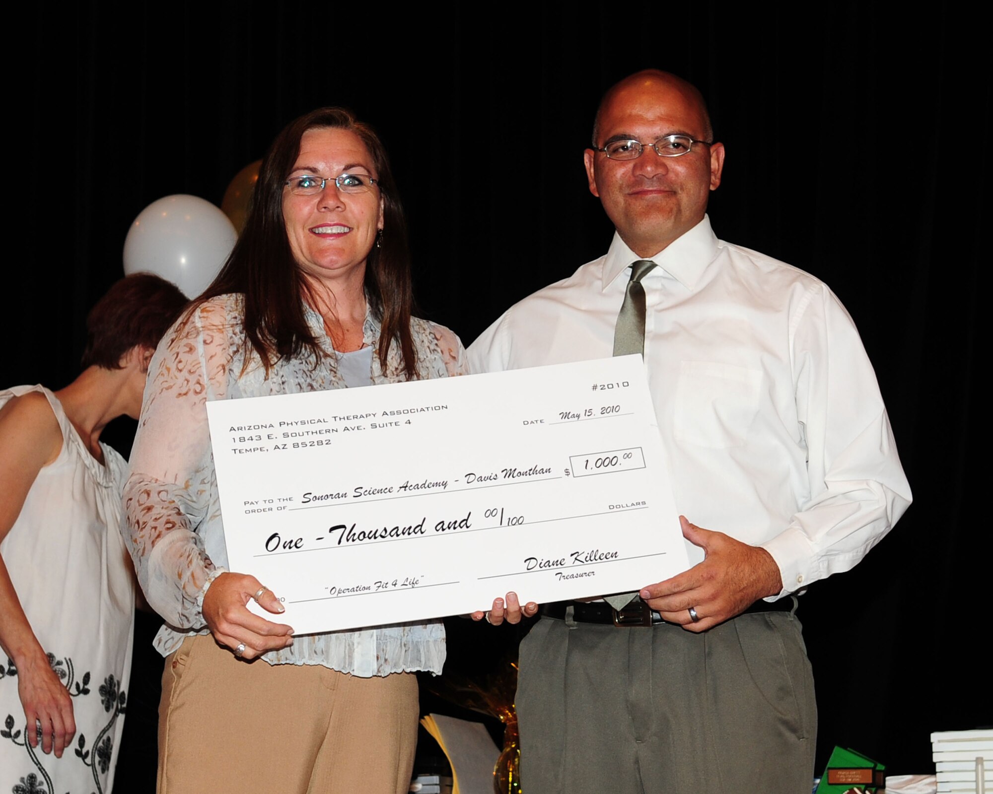Betsy Coyle presents a $1,000 grant to the Sonoran Science Academy on behalf of the Arizona Physical Therapy Association at the base theater here May 18. Funds will be used to form a cycling club in an effort to promote disability awareness throughout the school year. (U.S. Air Force photo/Airman Jerilyn Quintanilla)
