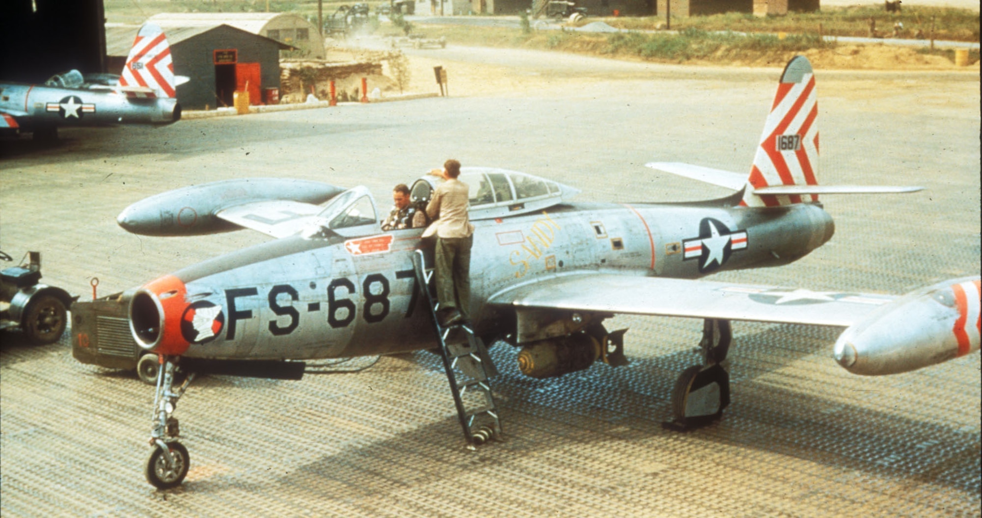 F-84 crew chief cleans the canopy as the pilot straps in before a mission. (U.S. Air Force photo)