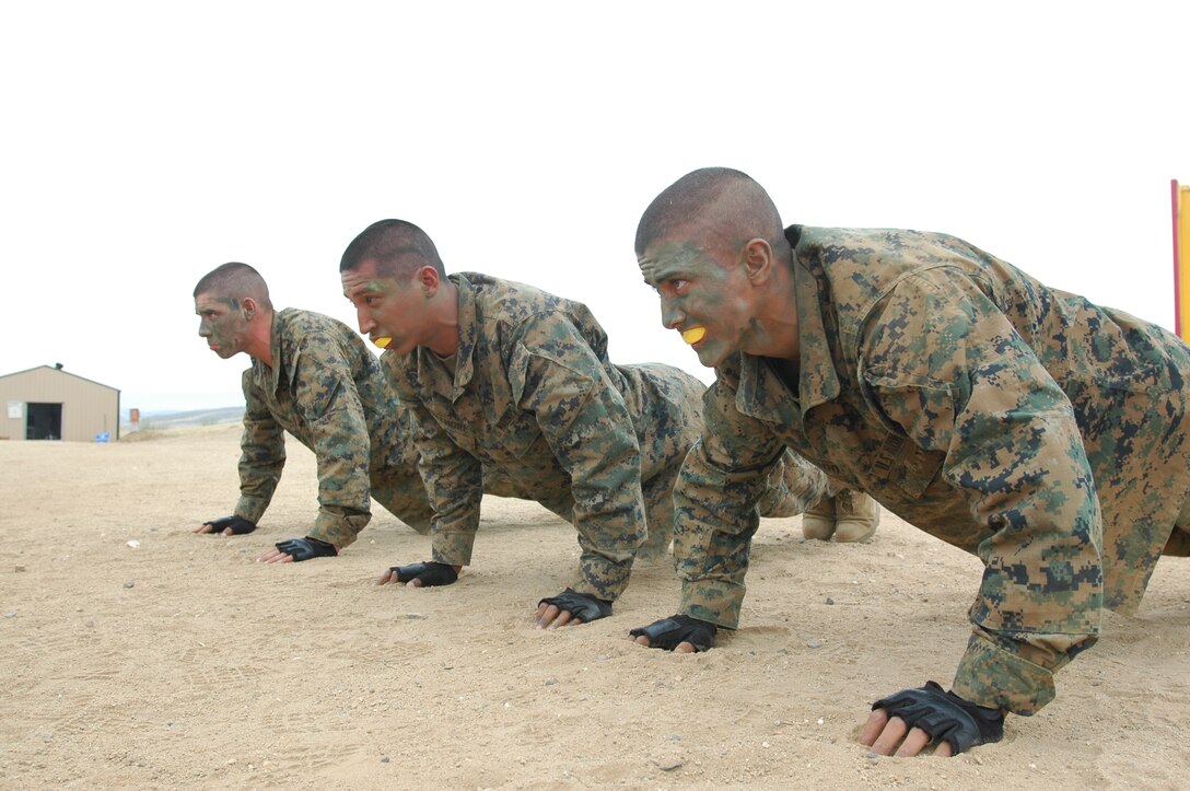 From left to right, recruits Michael Tighe, Anthony Whitmore and Romancory Querido, Platoon 3215, get on their faces and push at one of the exercise stations surrounding the body sparring ring to simulate combat stress.
