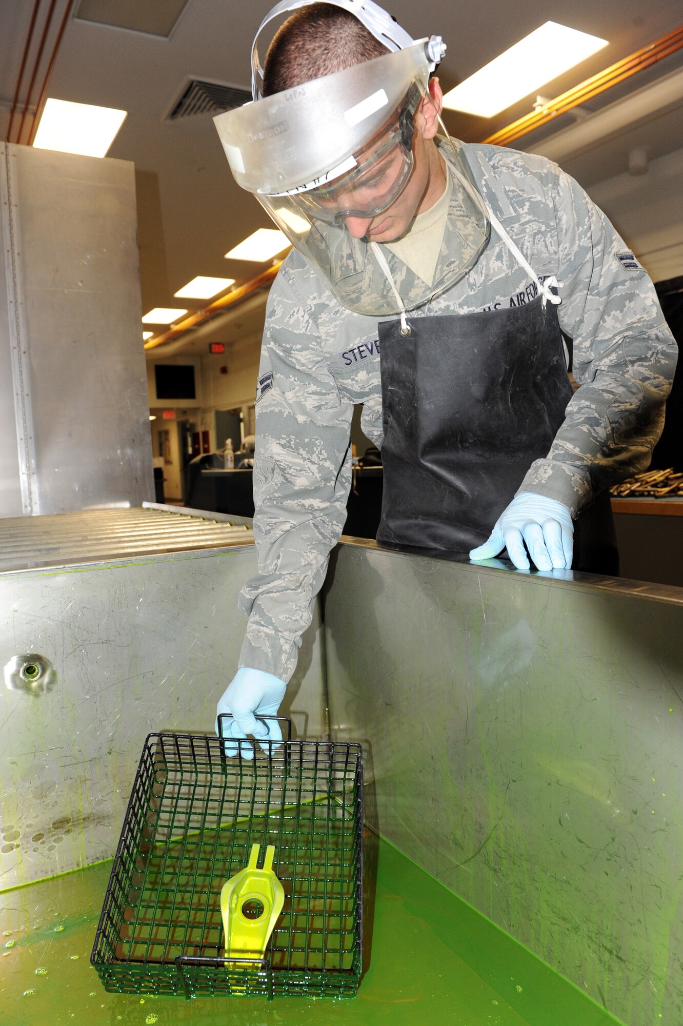 Airman 1st Class John Stevens, 19th Equipment Maintenance Squadron non-destructive inspection journeyman, dips a tow fitting arm in a fluorescent liquid penetrant June 4 during a fluorescent liquid penetrant inspection at the base non-destructive inspection lab. Suspected damaged pieces of equipment are placed in the fluorescent liquid penetrant, which is then left to sit for 30 minutes so that the penetrant has time to be absorbed into any cracks that may be present. (U.S. Air Force photo by Senior Airman Ethan Morgan)