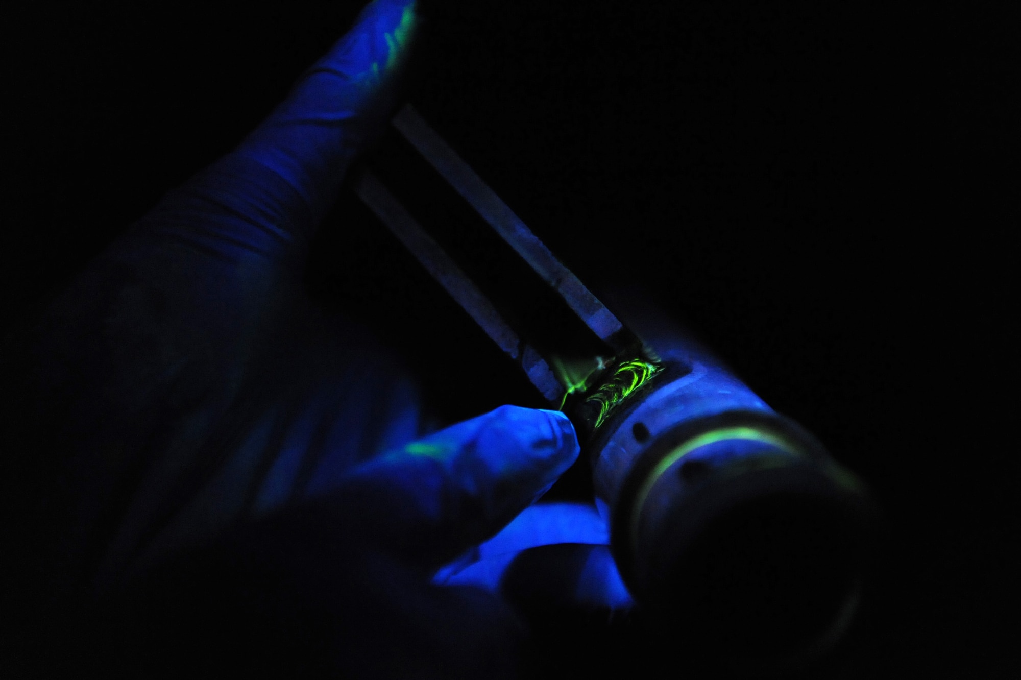 Airman 1st Class Ashton Surber, 19th Equipment Maintenance Squadron non-destructive inspection journeyman, points out a crack on a tow fitting crossbar June 4 during a magnetic particle inspection at the base non-destructive inspection lab. The crack is distinguished by a bright glow when placed under a black light. (U.S. Air Force photo by Senior Airman Ethan Morgan)