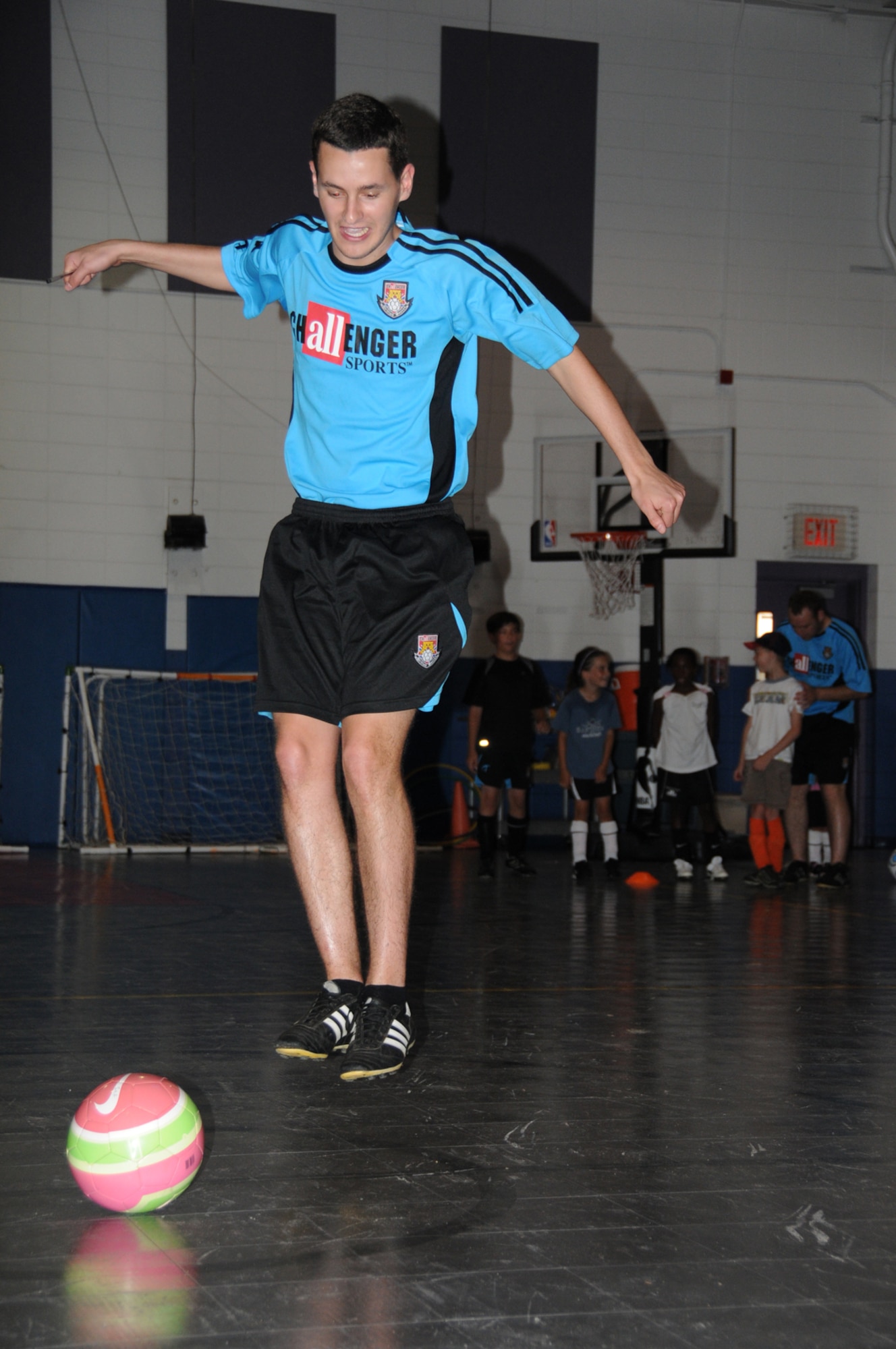 Instructor James Hamouda demonstrates how to perform a drill during the first day of the Challenger Sports British Soccer Camp at the youth center gym Monday.  The camp for ages 4-18 had to be moved inside because of “black flag” weather conditions.  (U.S. Air Force photo by Kemberly Groue)