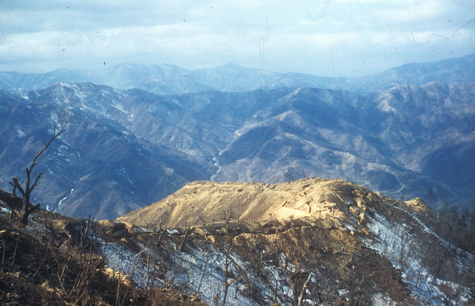 Desolate UN trench line along the mountainous 38th Parallel (also called the Main Line of Resistance or MLR). Heartbreak Ridge, a fiercely contested position, is visible in the background. (U.S. Air Force photo)