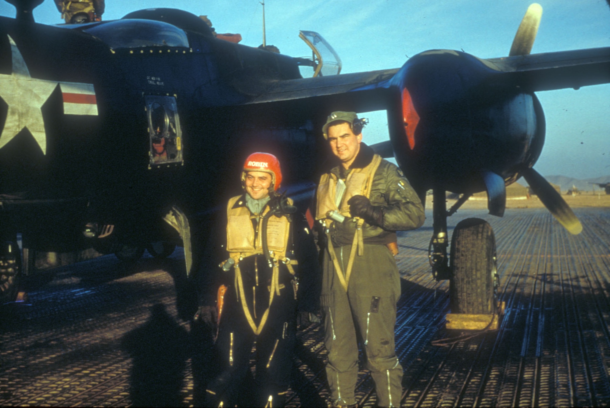 As the sun sets, Maj. Robert Fortney and Capt. Bob Dorbacker stand fully outfitted for the night's mission. Their aircraft is painted black for camouflage at in the dark. (U.S. Air Force photo)