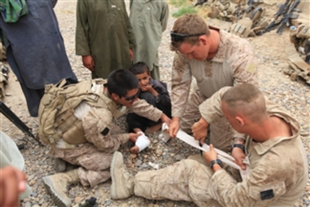 U.S. Navy Petty Officer Dan Royston (2nd from right) and Marine Corps Lance Cpl. Kaleb Hyndman (left) both with Weapons Company, 3rd Battalion, 1st Marine Regiment, 1st Marine Division put a bandage on an injured boy near Patrol Base Gorgak, Afghanistan, on May 16, 2010.  