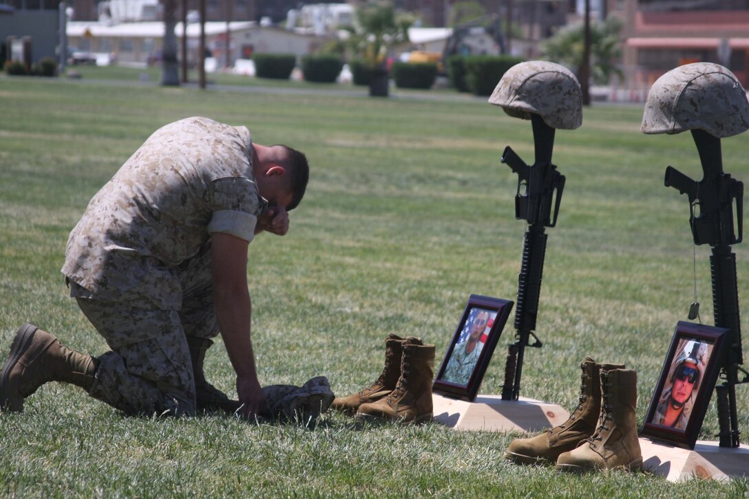 During a memorial service June 11 at Lance Cpl. Torrey L. Gray Field, Sgt. Brandon Jansen kneels at the memorial of Lance Cpl. Cody Stanley who sacrificed his life while attempting to save another Marine in Helmand province, Afghanistan. Jansen was Stanley’s section leader in Weapons Company during the deployment.::r::::n::