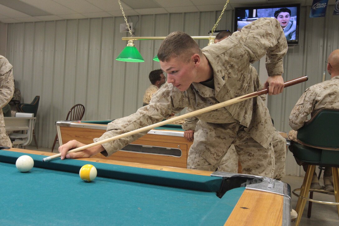 Lance Cpl. Christopher Burrage, an amphibious assault vehicle crewman for Headquarters and Service Co., 3rd Amphibious Assault Battalion, relaxes and shoots pool with fellow Marines at the Warriors Club June 11. ::r::::n::