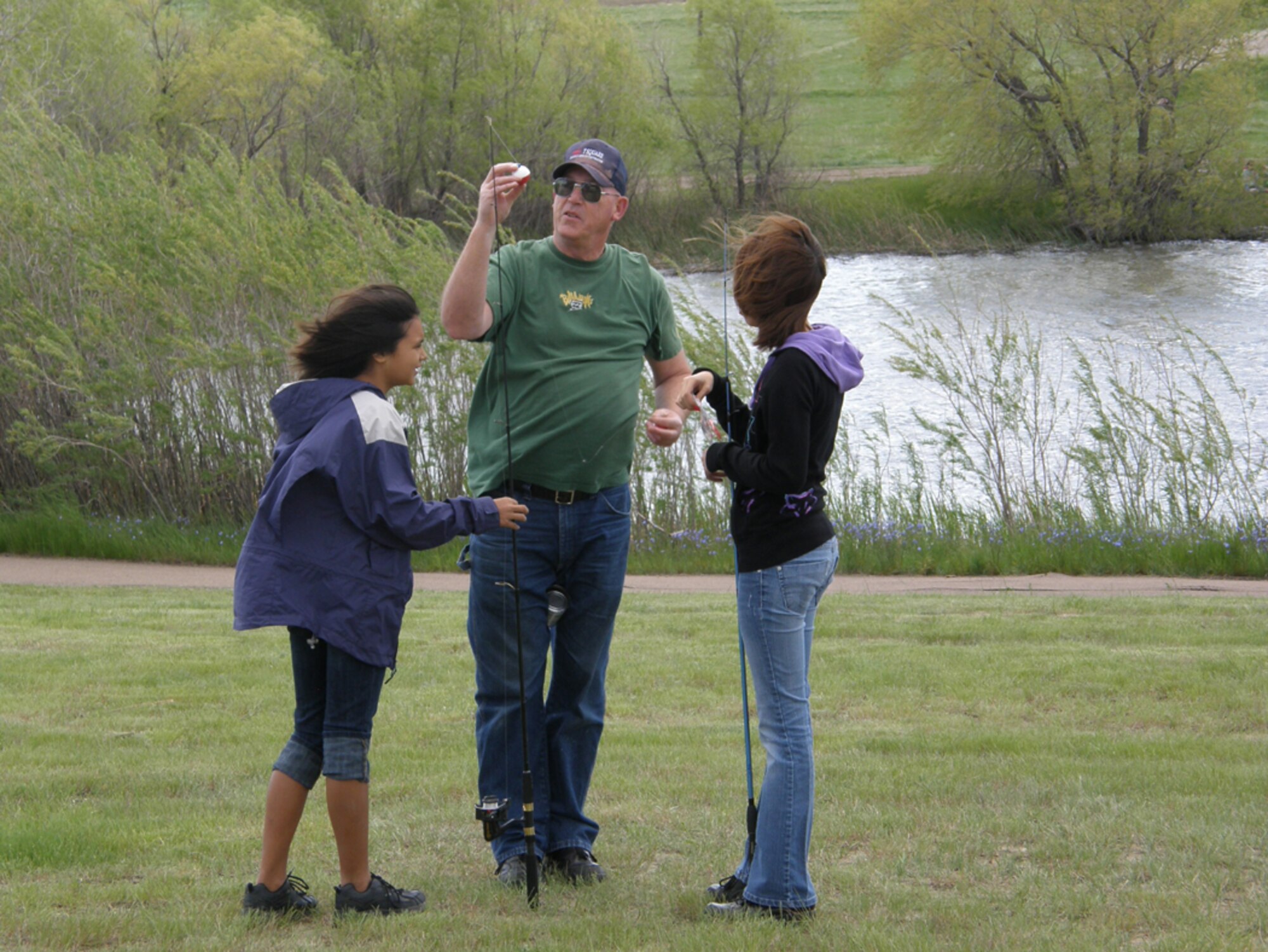 Gordon Truesdell helps grandaughters Asia Gratreaks, 11 (left) and Tristin Rose, 12, attach bobbers to their fishing poles during the National Kid's Fishing Day June 5 at Malmstrom. (Courtesy photo)