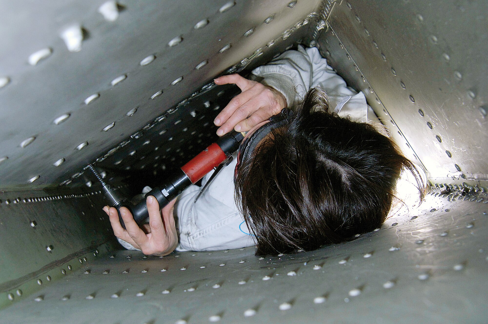 At 5-foot 2-inches tall and little more than 100 pounds, sheet metal mechanic Hien Nguyen thought she could fit into a Navy E-6 wing space, do the necessary fasteners work and save her co-workers many hours that before were spent removing and re-attaching sheet metal to get to the area. With a spotter outside the tight space helping her, she works this part of the SLEP modification that is strengthening the jet’s wings. (Air Force photos by Margo Wright)