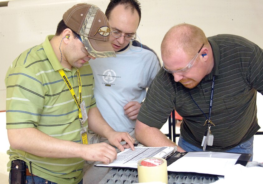Service Life Extension Program supervisor Pascual Villegas (from left) discusses aircraft work with Sheet Metal Mechanics Jonathan Robidoux and Jason “Red” Timm under the wing of one of the first jets to receive the modification work at Tinker AFB, Okla. (U.S. Air Force photo/Margo Wright)