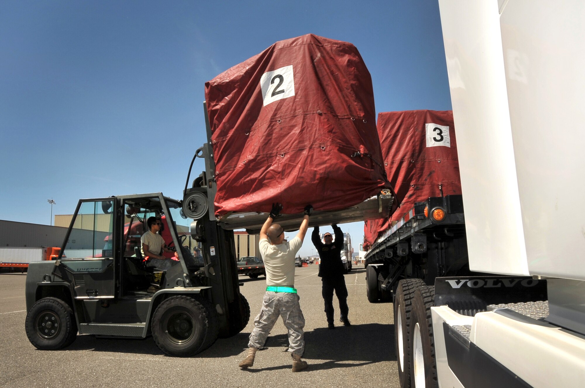 Airman First Class Takuya Oshiro, 60th Aerial Port Squadron, and Mr. Paul Coggiola of the Sacramento Urban Search and Rescue team assist fork lift driver, Airman First Class Jeffery Rivera, 60th Aerial Port Squadron, as he prepares to move cargo off truck trailers so that it can be measured and weighed to make sure it fits within aircraft loading requirements. (U.S. Air Force photo by Civ/Amanda Lopez)
