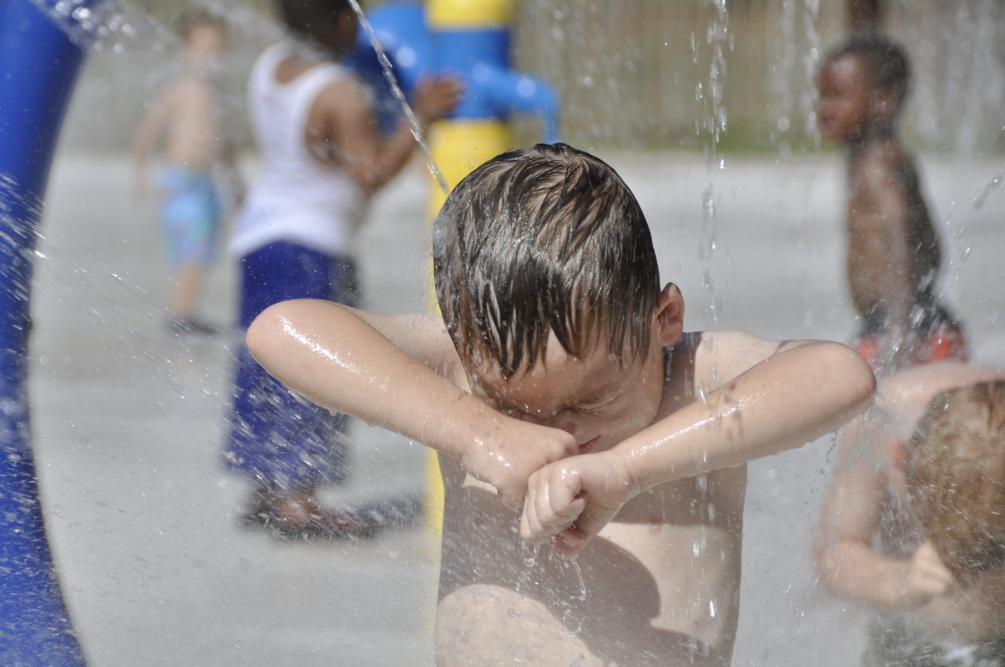 Stratos Bennett, 5, shields himself from water spraying all around him at Eglin's splash pad located in Unity Park. The Child Development Center takes students to the park regularly as a means to cool down during the summer. (U.S.Air Force photo/Chrissy Cuttita)