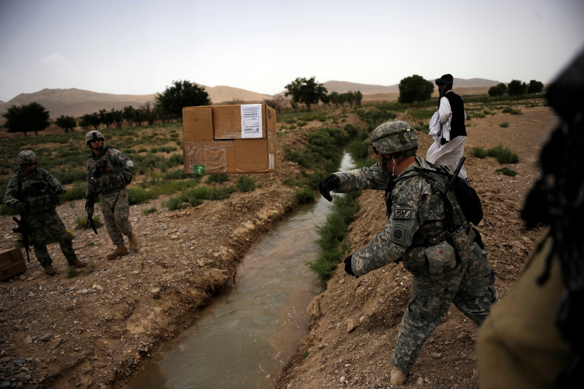 A Soldier assigned to Provincial Reconstruction Team Zabul throws a box of coloring books across an irrigation canal on the way to the Omarkhel Village for a Shura May 22, 2010, in Zabul Province, Afghanistan. (U.S. Air Force photo/Staff Sgt. Manuel J. Martinez/released) 
