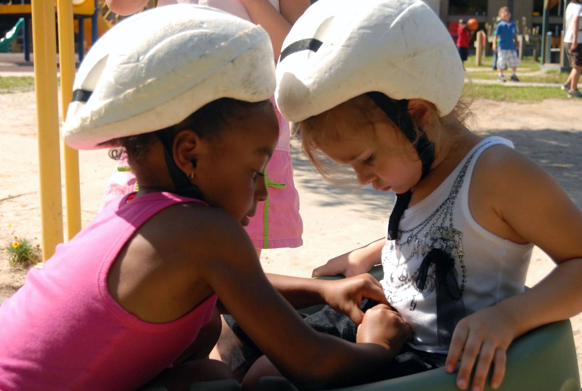 Deija Hyder, 5, (left) helps Cheyenne Grier, 4, buckle her safety restraint June 11 at the Child Development Center, here. Playground safety is an added consideration during the 101 Critical Days of Summer, historically observed each year between Memorial Day and Labor Day. (U.S. Air Force photo/ 1st Lt. Cammie Quinn) 