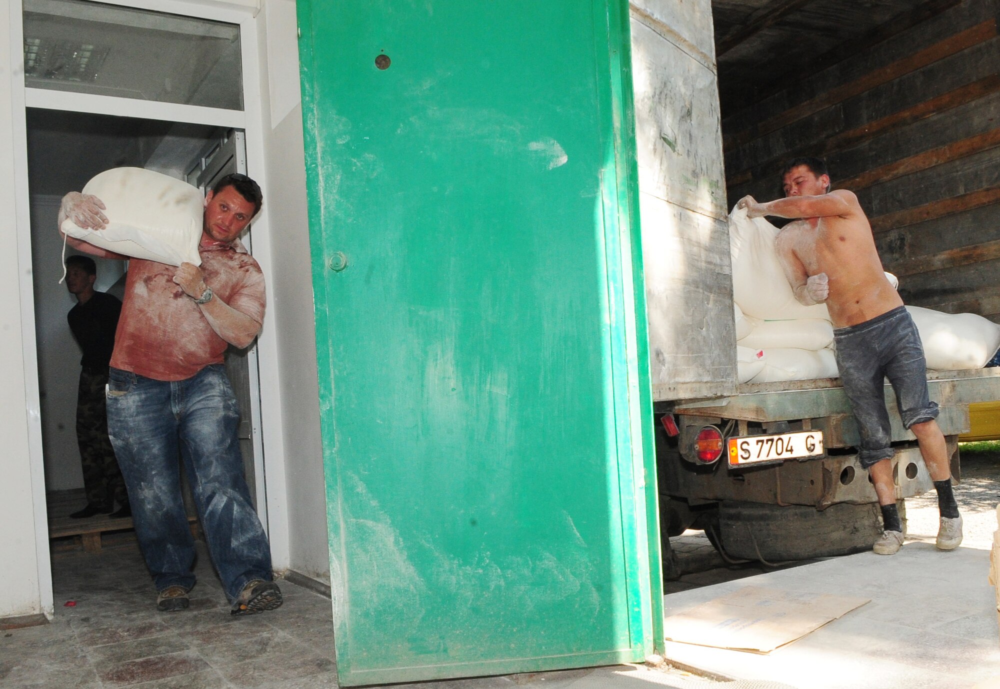 Staff Sgt. Yevgeniy Maksimov, 376th Air Expeditionary Wing coalition coordinator linguist, carries flour as a Kyrgyz youth assists by loading it onto a delivery truck in Bishkek, Kyrgyzstan, June 13, 2010.  The Transit Center at Manas, together with the U.S. Department of State, purchased nearly $9,000 worth of food for a humanitarian assistance delivery to the southern region of Osh.  (U.S. Air Force photo/ Senior Airman Nichelle Anderson/ released)