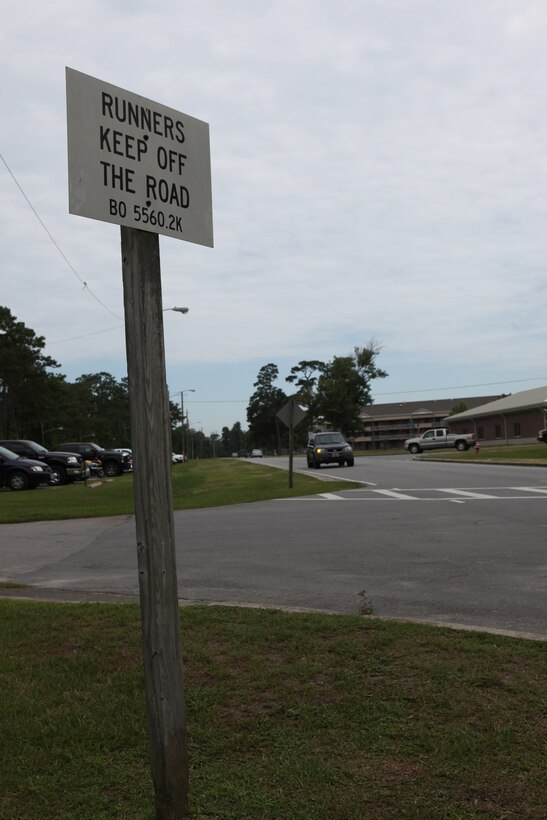 A sign on Julian C. Smith Road aboard Marine Corps Base Camp Lejeune reminds runners to maintain a safe distance from oncoming traffic.  Runners may run on Julian C. Smith Road, from Cross Street to O Street, from 6:00 to 8:00 a.m., Mondays through Fridays, but must use running paths or stay at least six feet away from the road at all other times.