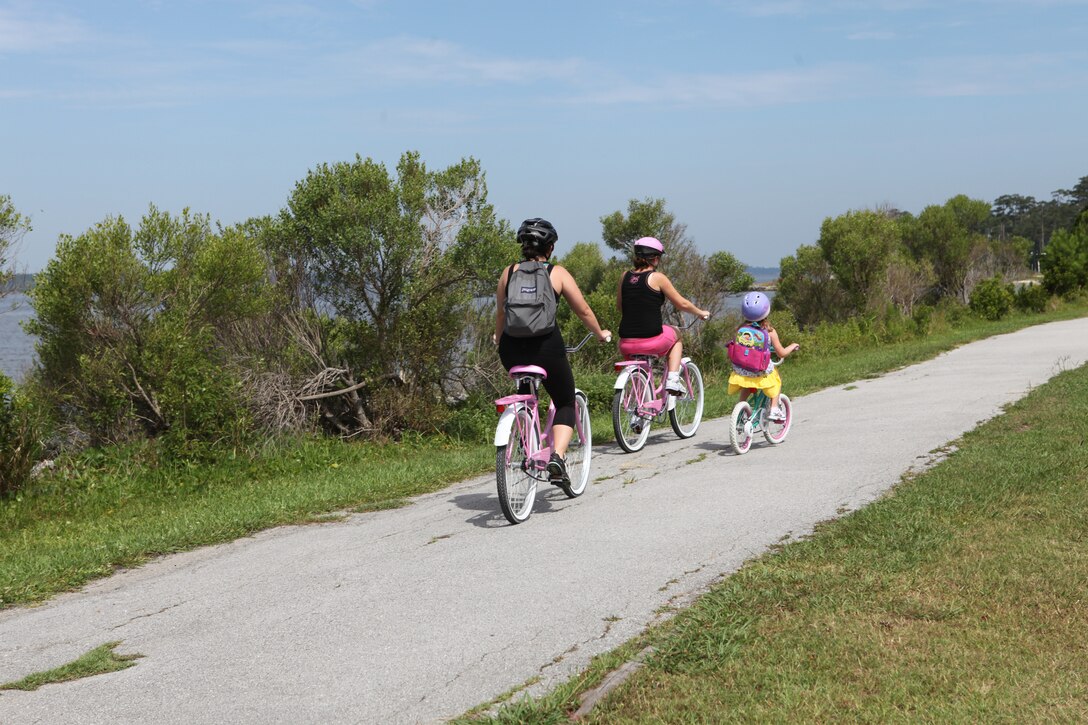 Bicyclists pedal alongside the river on a running trail parallel to Julian C. Smith Road aboard Marine Corps Base Camp Lejeune, June 15.  Although Julian C. Smith Road, from Cross Street to O Street, is closed from 6:00 to 8:00 a.m., Mondays through Fridays, to allow for large units and individual physical training sessions, running paths are often utilized as a safe alternative.