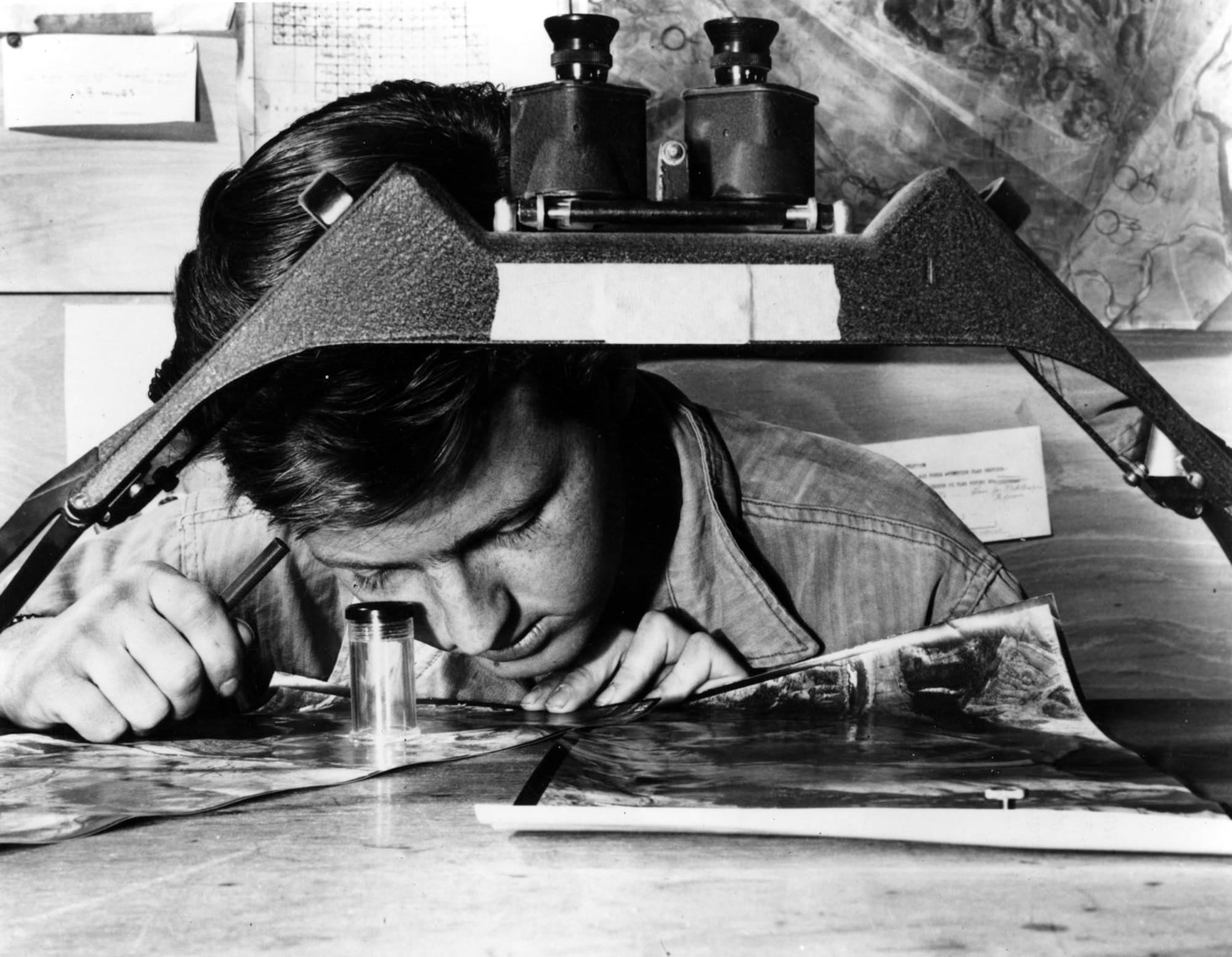 Sgt. James Kindseth examines communist anti-aircraft positions through a magnifying loupe. In the foreground is a well-equipped stereoscope. (U.S. Air Force photo)