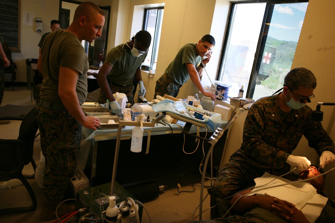 Cmdr. Thomas Olivero, a dental officer with 4th Marine Logistics Group, fills a patient's tooth while his staff looks on.