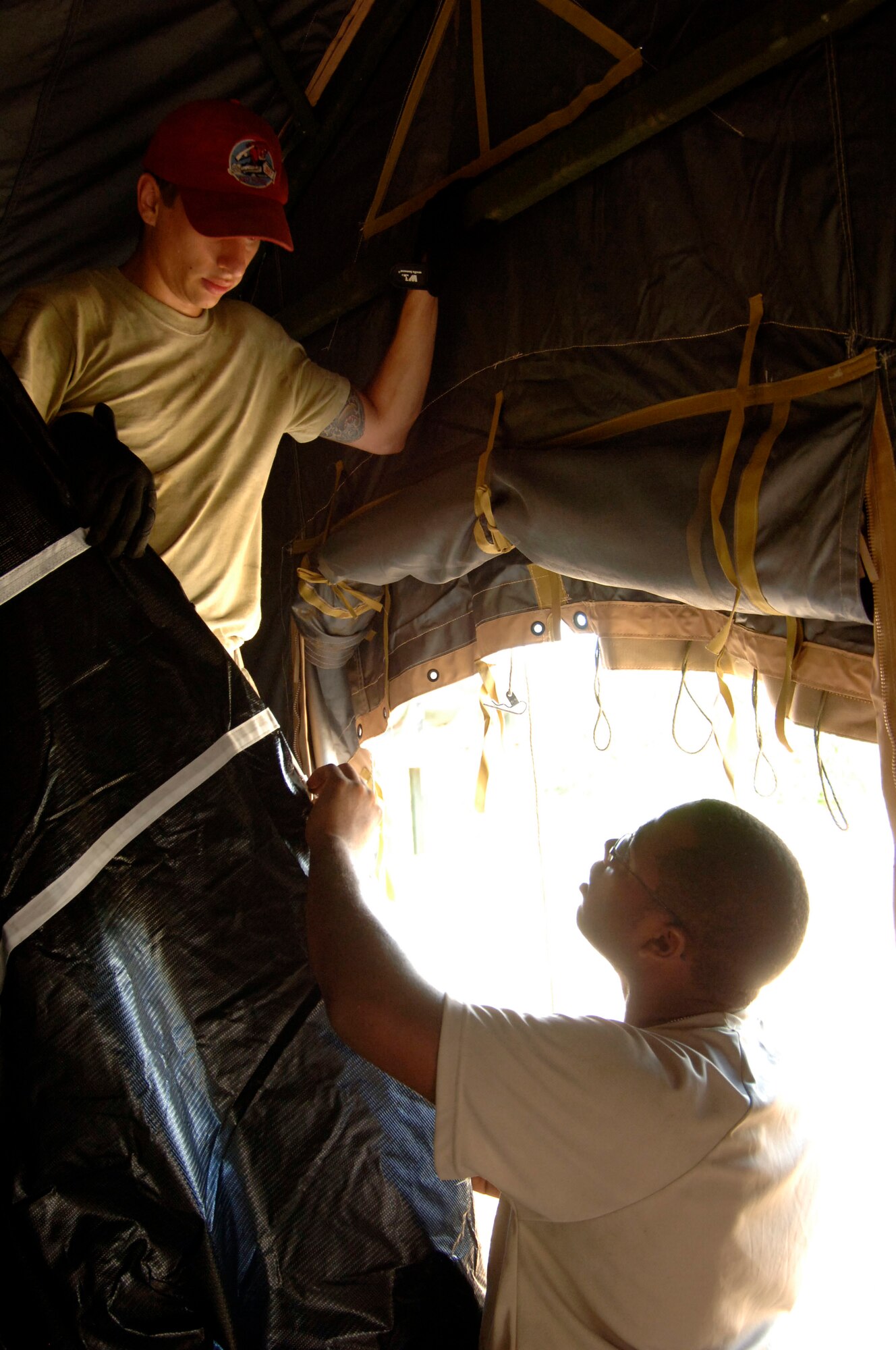 Senior Airmen Phillip Conroy (left) and Markiss Hines, 567th RED HORSE Squadron, install the inner liner to a tent at the temporary encampment that will house more than 250 Airmen, Soldiers, and Marines for New Horizons Panama 2010. (U.S. Air Force photo/Tech. Sgt. Eric Petosky)