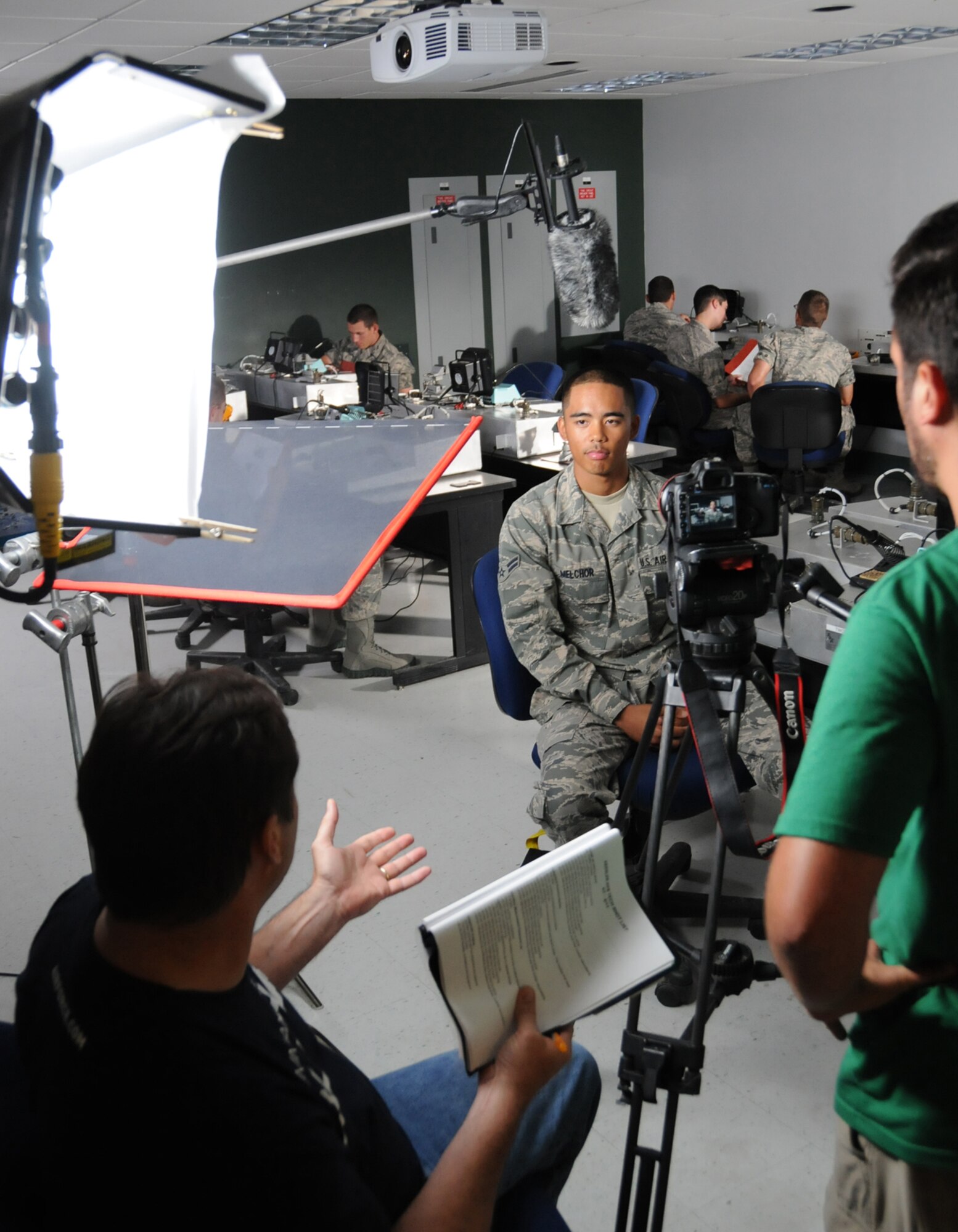 Creative director Tom Gilmore, left, interviews Airman 1st Class Christopher Melchor, a student in the 332nd TRS electronic principles course, as classmates in the background prepare work stations for troubleshooting faulty wire connections in Dolan Hall June 8.  The project is intended to highlight various lifestyle aspects at Keesler.  The shoot focused on interviews with members of Team Keesler, especially students, and highlighted base facilities.  (U.S. Air Force photo by Kemberly Groue)
