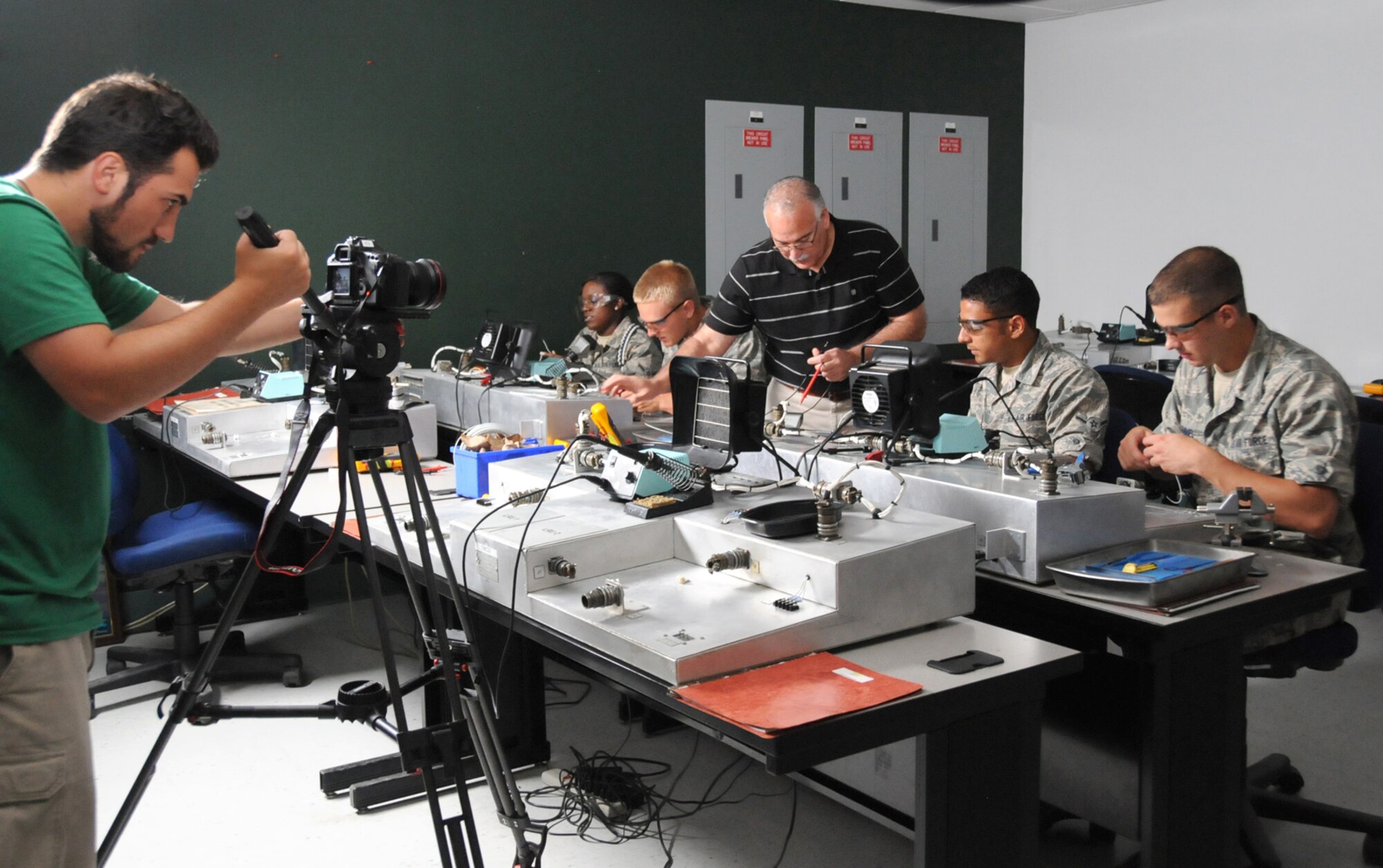 Videographer Julio Quintana films as 332nd Training Squadron electronic principles instructor Steve Hall (standing) shows his students procedures associated with soldering multipin connectors and terminal lug connections in Dolan Hall June 8.  From left, students are Airman Nakia Bracey, Airman Basic Alan Tomaszycki, Airman Kevin Saravia and Airman Basic Kevin Gummel.  A film crew from GSD&M in Austin, Texas, spent four days at Keesler to film footage for the Air Force Recruiting Service.  The final product will include footage from Keesler and other training bases to refresh portions of the recruiting service’s national Web site at airforce.com.  (U.S. Air Force photo by Kemberly Groue)
