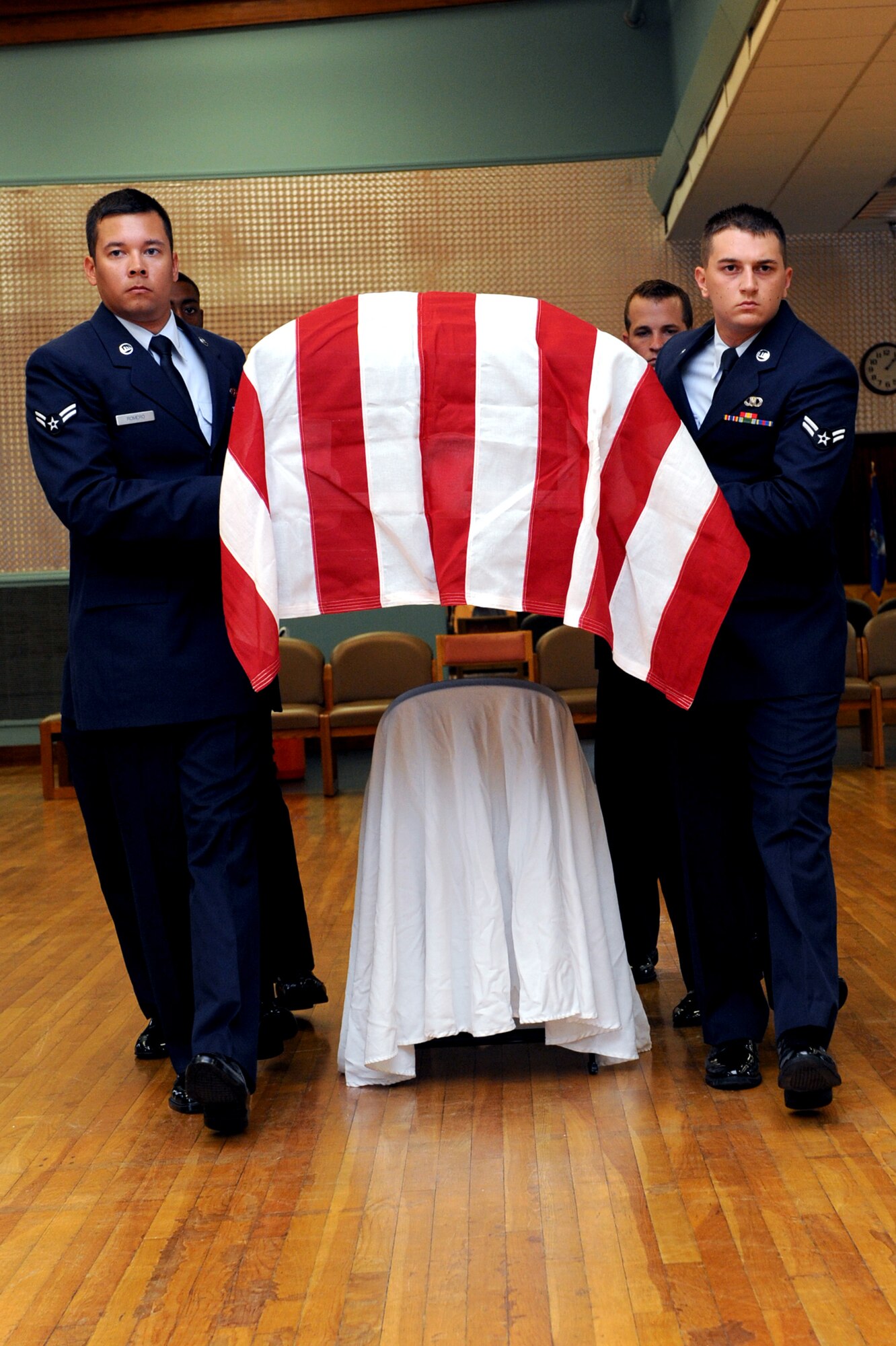 The newest members of the Little Rock Air Force Base’s Honor Guard lift a casket over a chair June 14 during a mock funeral ceremony at the Honor Guard graduation at the Thomas Community Activities Center. The chair was used to represent a headstone they would have to maneuver around in a real funeral ceremony. (U.S. Air Force photo by Senior Airman Ethan Morgan)