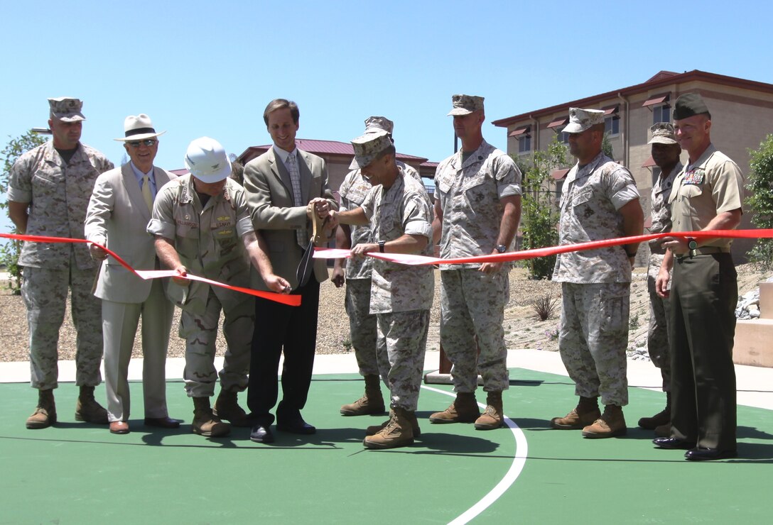 Navy Capt. Michael Williamson (white hard hat), officer in charge of construction, Marine Corps Installations West; Jeff Harper (black slacks), president of Harper construction; and Col. Nicholas F. Marano (holding scissors), commanding officer, Marine Corps Base Camp Pendleton, accompanied by other Department of Defense employees and contractors, cut the ribbon during an opening ceremony for five newly completed bachelor enlisted quarters at Camp Pendleton, June 16. The $122 million BEQs, include natural gas and charcoal BBQ grills, washing stations for equipment, bike lockers, horseshoe pits and volleyball and basketball courts. The five barracks have taken an estimated 413,448 man-hours to complete, include 876 rooms and can house 1,752 Marines.