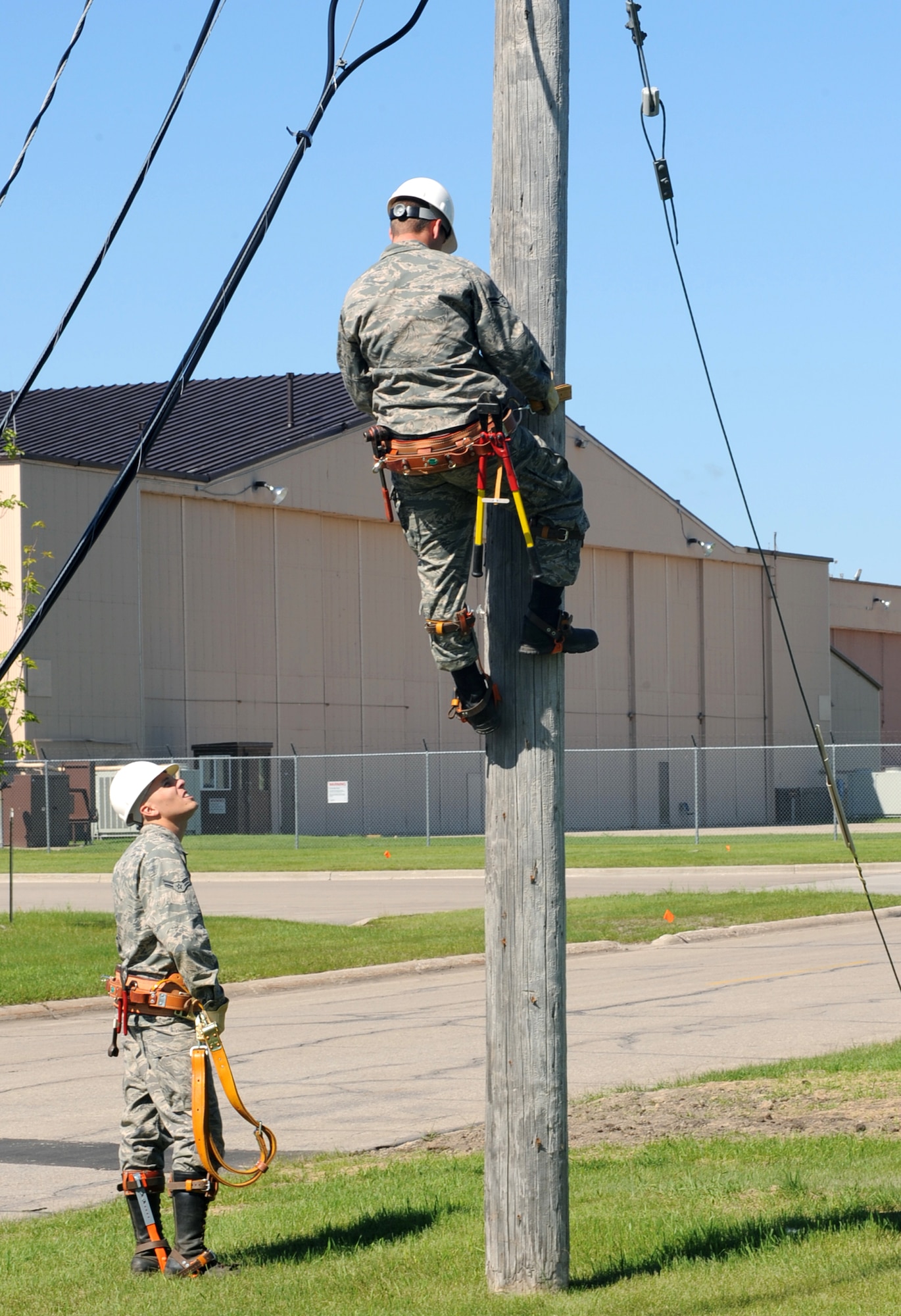 An Airman from the 319th Civil Engineer Squadron watches as Airman 1st Class Patrick McFadden, an electrical systems apprentice with the 319 CES, starts to climbs up an old telephone pole to deconstruct telephone lines here June 16. The 319 CES is in the process of deconstructing the old telephone pole lines due to the fact base telephone lines are now buried. (U.S. Air Force photo by Airman 1st Class Amber Price)