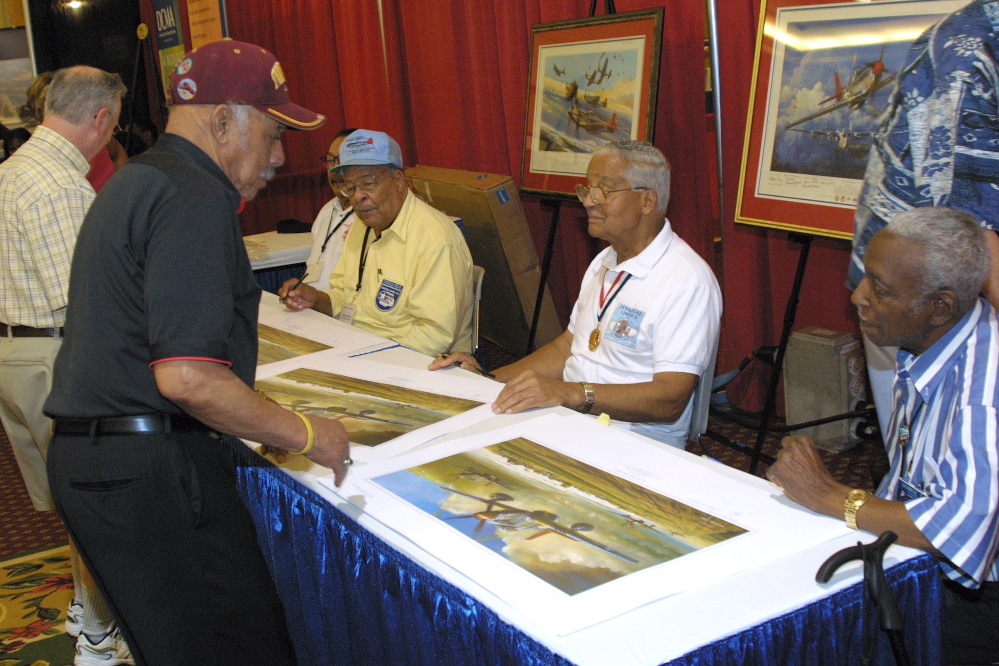 Five Tuskegee Airmen prepare to autograph lithographs Aug. 6, 2008, illustrating various missions the men flew during World War II. Retired Lt. Col. Bill Holloman (standing) went on to become the Air Force's first African-American helicopter pilot. Colonel Holloman died June 11, 2010, in Kent, Wash.