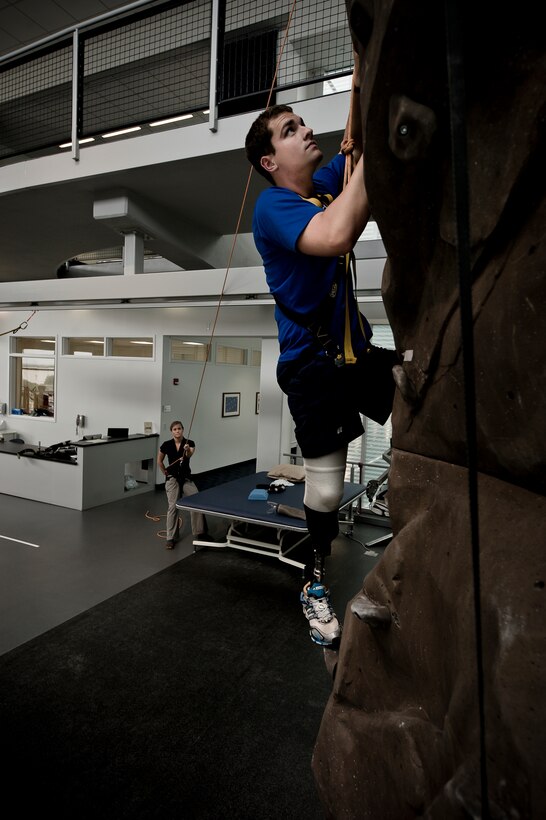 Conquering the rock climbing wall at the Center for the Intrepid is just one of the exercises physical therapist Alicia White (holding the safety rope) has McGuire perform. The rehabilitation therapy helps the lieutenant get used to the prosthetic he received after having his lower right leg amputated following a boating mishap last summer.(TSgt Samuel Bendet)