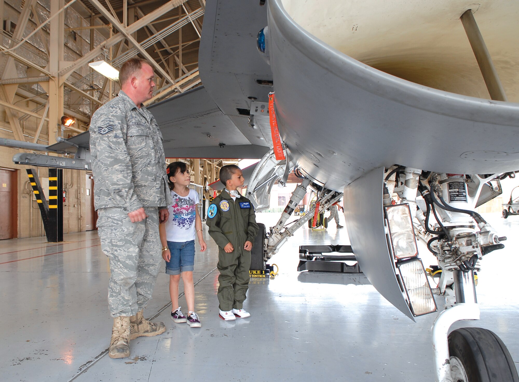 Staff Sgt. Jerry Tucker, 309th Aircraft Maintenance Unit crew chief, gives Zuriah Acosta and Isaiah Acosta, pilot-for-a-day, a tour of an F-16 Fighting Falcon June 11 in Hangar 914. (Photo by Airman 1st Class Ronifel Yasay)