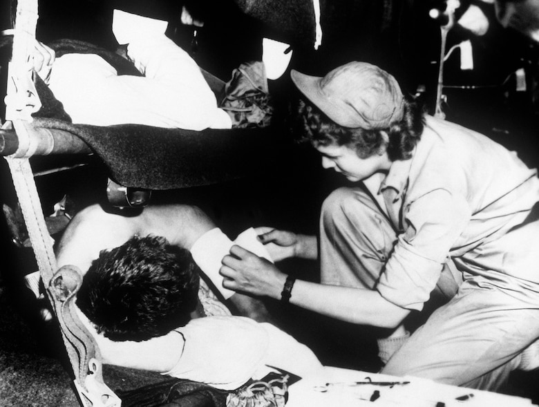 A U.S. Air Force Nurse Corps flight nurse dresses a patient’s wound during an aeromedical evacuation flight from Korea to Japan, May 1951. (Courtesy photo)