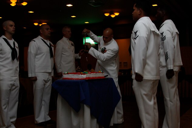Chief Adrian Figueroa, hospital corpsman ball guest speaker, cuts the cake during the hospital corpsman cake cutting ceremony at the Club Iwakuni Eagles Nest here June 18. After cutting the cake, Figueroa passed the first slice to Chief Simeon Cadavos, oldest corpsman present at the ceremony, and Seaman Zachary Hallowood, youngest corpsman present at the ceremony.