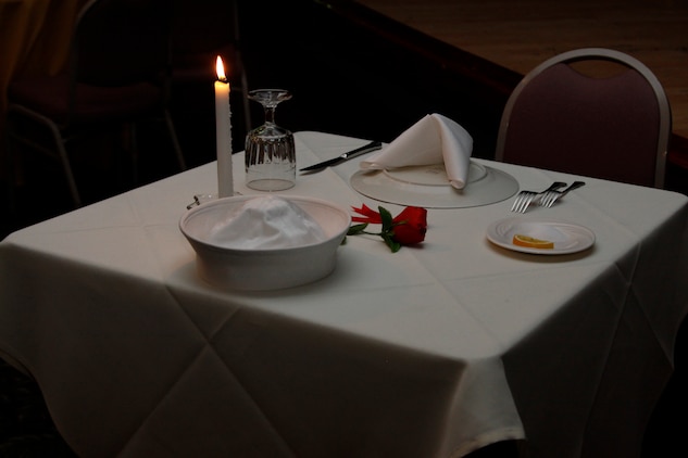 This table was set aside in honor and reverence of all men and women prisoners of war from all services during the Hospital Corpsmen Ball hosted at the Club Iwakuni Eagles Nest here June 18. The white table cloth symbolized the purity of their intentions in responding to their country’s call to arms so their children could remain free. The burning candle symbolized the frailty of a prisoner alone standing up to his oppressors. The red ribbon was a symbol of those who would not return home, and the rose symbolized the hope of the family members who await their return home. A slice of lemon symbolized the prisoner’s bitter fate if he is never brought home, while salt on the plate symbolized the tears shed by family members awaiting the prisoner’s return home. The glass turned upside down symbolized the prisoners inability to toast everyone else.