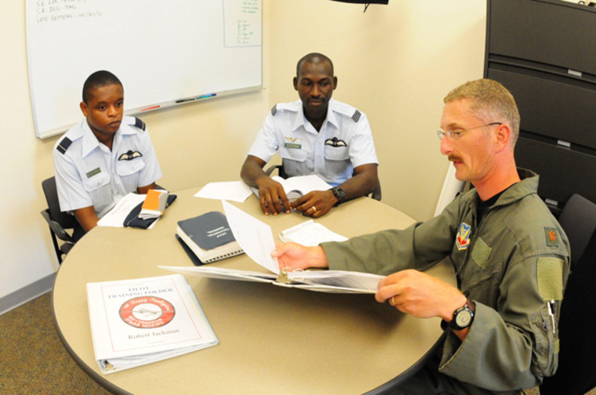 North Dakota Air National Guard pilot Maj. Steven Larson, right, explains aspects of U.S. Air Force pilot training June 21, with visiting Ghanaian Air Force pilots Flying Officer Peter Attah-Obeng, left, and Flight Lieutenant Felix Kattah at the Fargo, N.D. Air National Guard flying wing.  The pilots are interacting as part of the state partnership program between the North Dakota National Guard and the African country of Ghana.