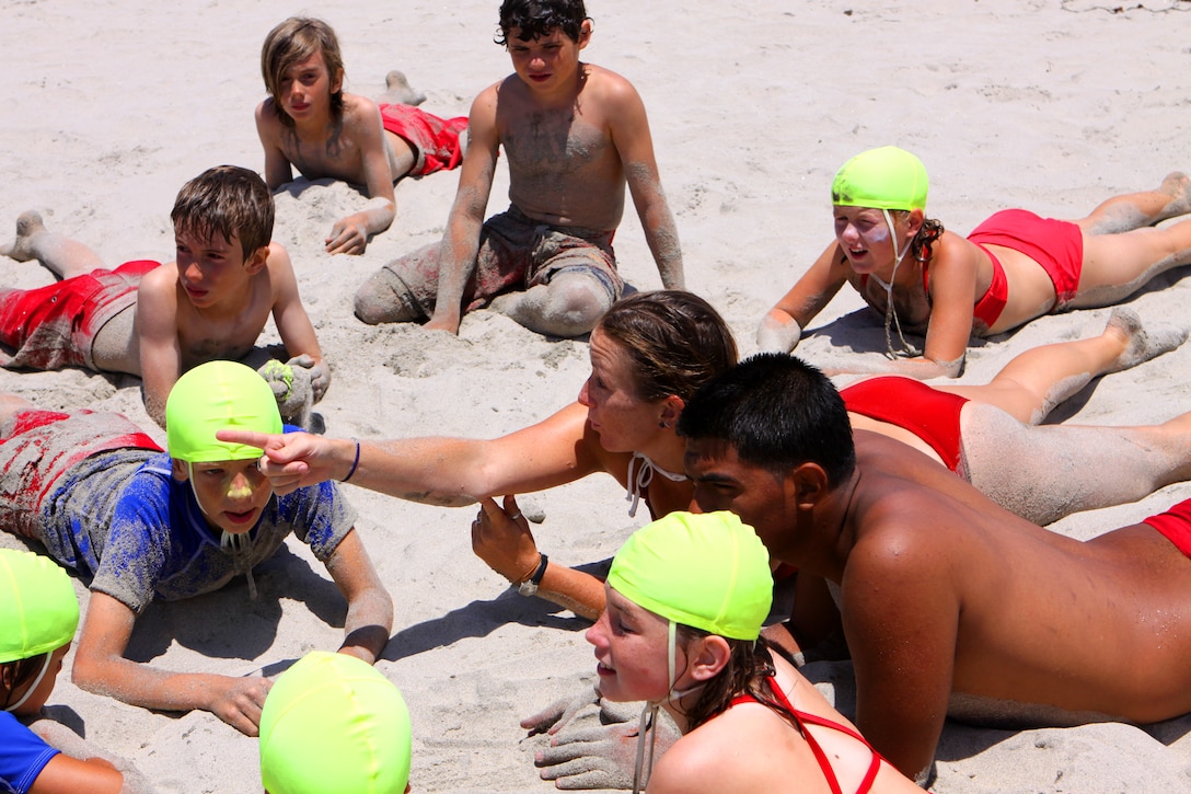 Lauren N. Ochsner (pointing), Junior Lifeguard Program instructor, Camp Pendleton Lifeguard Service, speaks to a group of military children during the first day of Camp Pendleton’s Junior Lifeguard Program on the shore of Camp Del Mar’s beach, June 21. The Junior Lifeguard Program is a 6 week summer program that is dedicated to teaching military children, between the ages of 9 and 16, general lifeguard knowledge such as first aid, recognizing and evading rip currents, environmental issues, and caring for the beach.