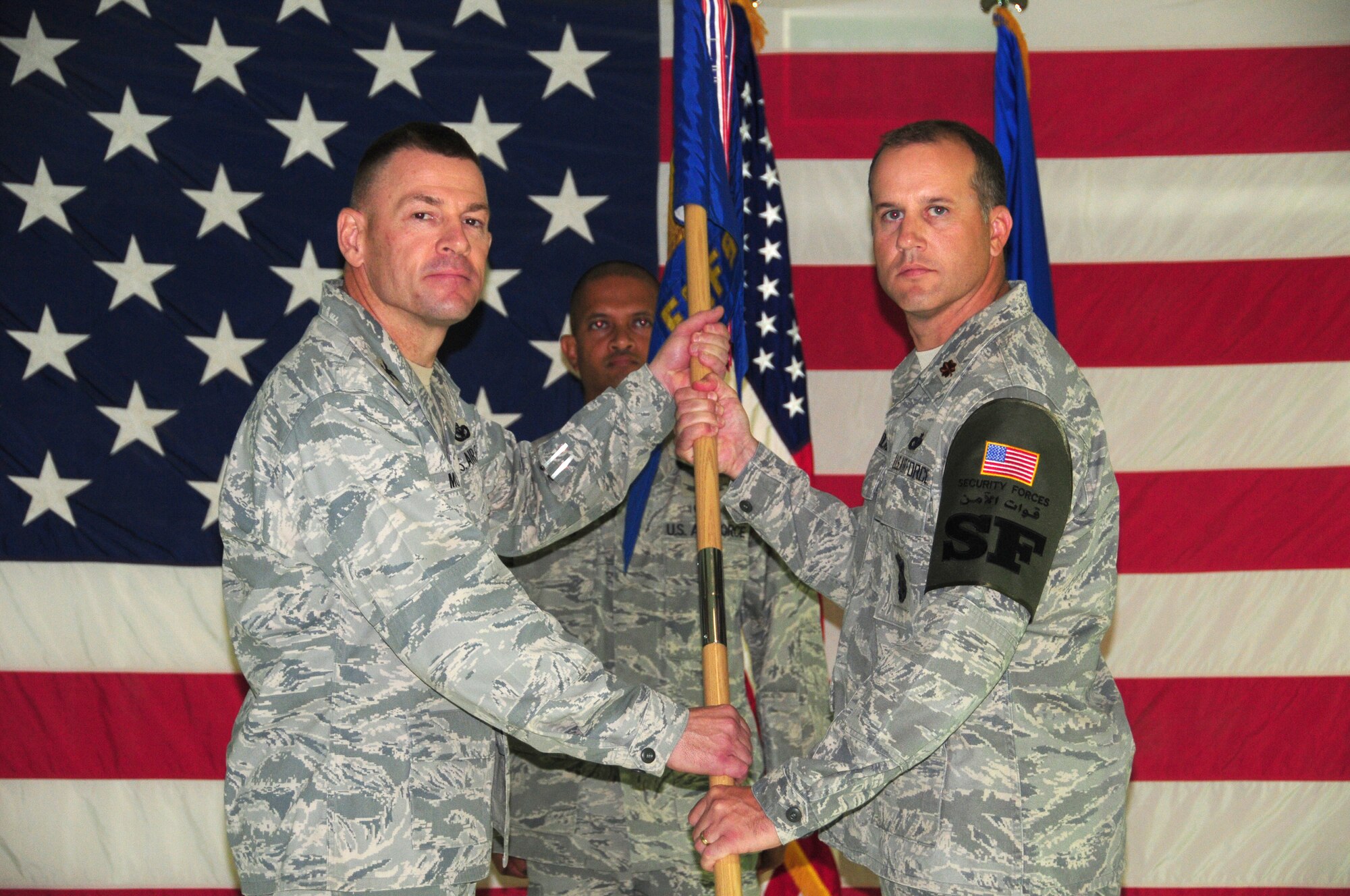 SOUTHWEST ASIA - From left, U.S. Air Force Col. Richard McComb, 386th Expeditionary Mission Support commander, passes the 386th Expeditionary Security Forces Squadron guidon to Maj. Philip Holmes, the new 386th ESFS commander, upon an assumption of command ceremony here June 22, 2010 at the base theater. Major Holmes assumed command after Lt. Col. John Oconnor relinquished command. (U.S. Air Force photo by Staff Sgt. Lakisha A. Croley/Released)