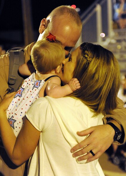 DYESS AIR FORCE BASE, Texas- Capt. Joshua Nimmo, 39th Airlift Squadron, with daughter Melody in arm, leans to give his wife, Jenny, a kiss here June 23 after returning from a six-month deployment supporting Overseas Contingencies Operations. Over 180 Airmen from the 317th Airlift Group, 7th Component Maintenance Squadron and 7th Logistics Readiness Squadron were greeted by family members, co-workers and friends. (U.S. Air Force photo/ Airman 1st Class Brittney Smolinski)